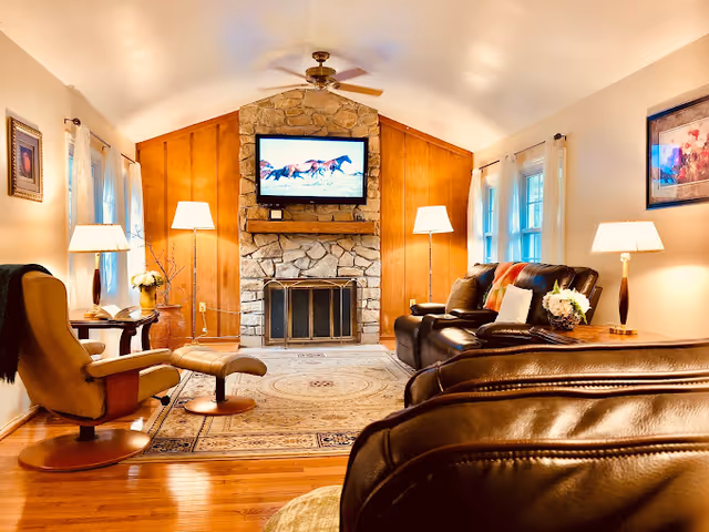 Cozy living room with stone fireplace, mounted TV, leather seating, and warm lighting.