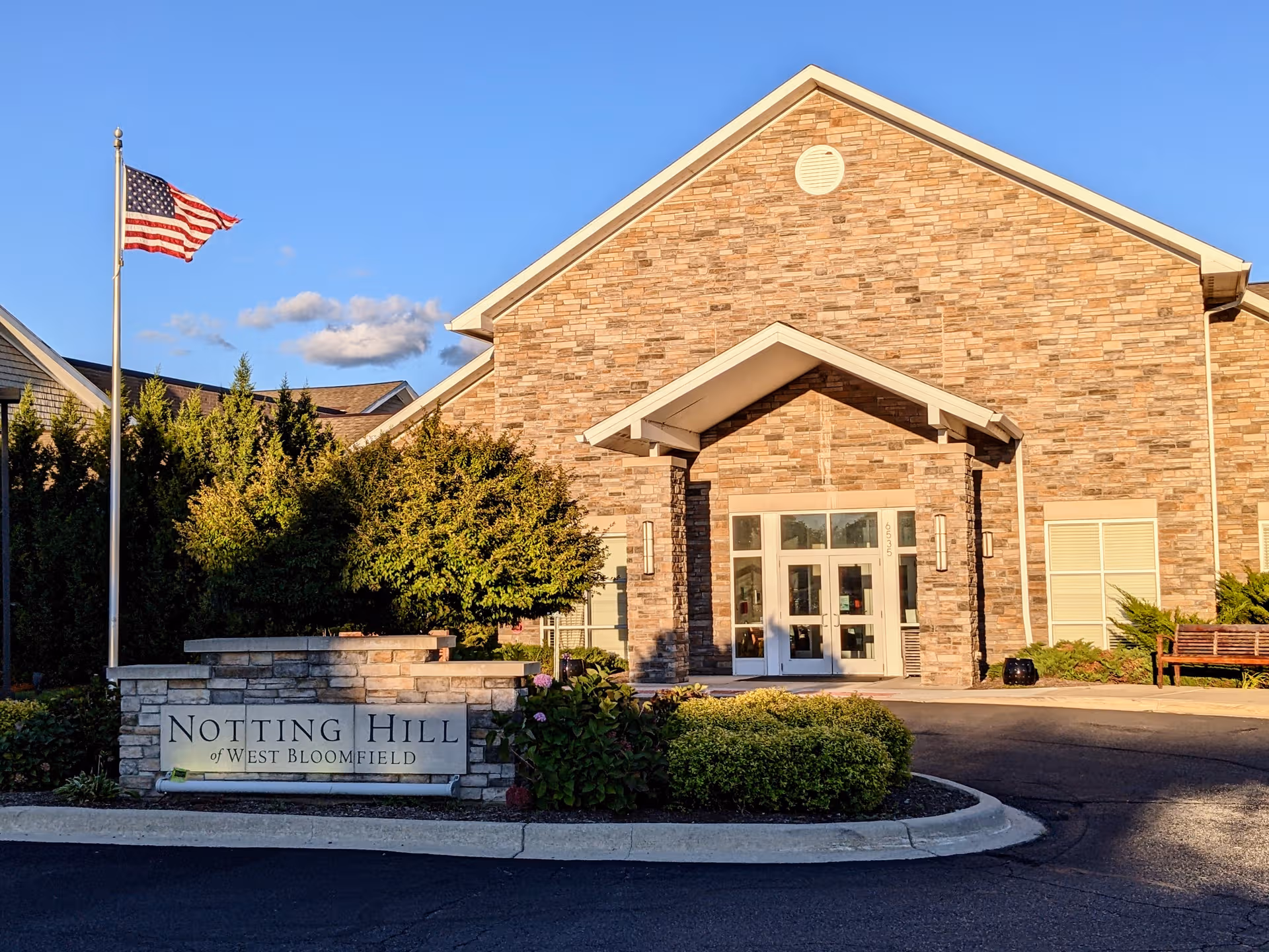 Front entrance of Notting Hill of West Bloomfield with brick facade, flag, and sign.