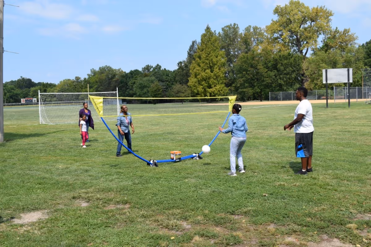 Group of people playing a game with a ball on a grassy outdoor field.