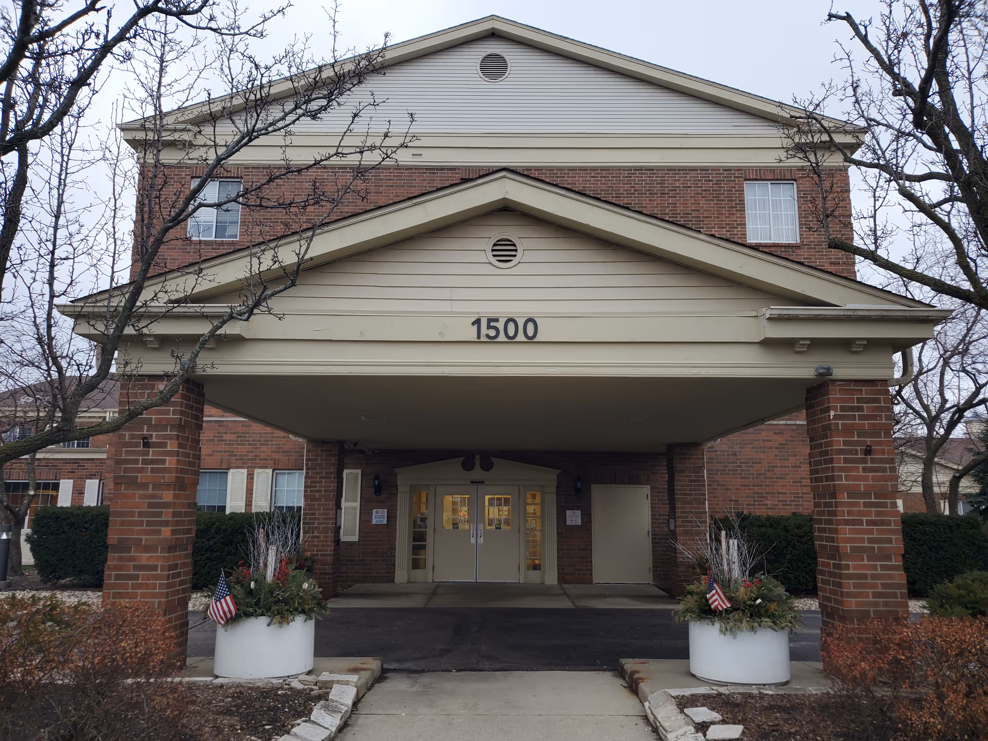 Brick senior living entrance with a wide covered drop-off and address 1500