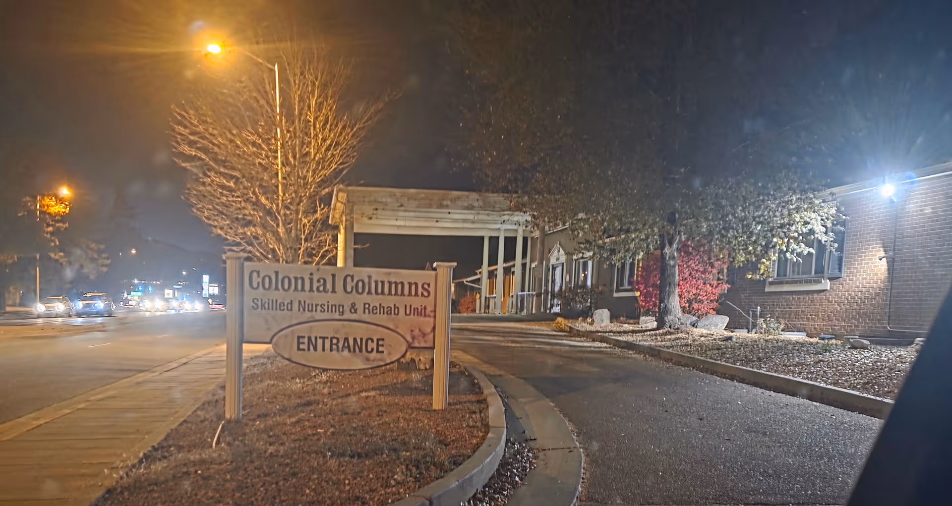 Nighttime exterior view of Colonial Columns entrance with sign and landscaping.