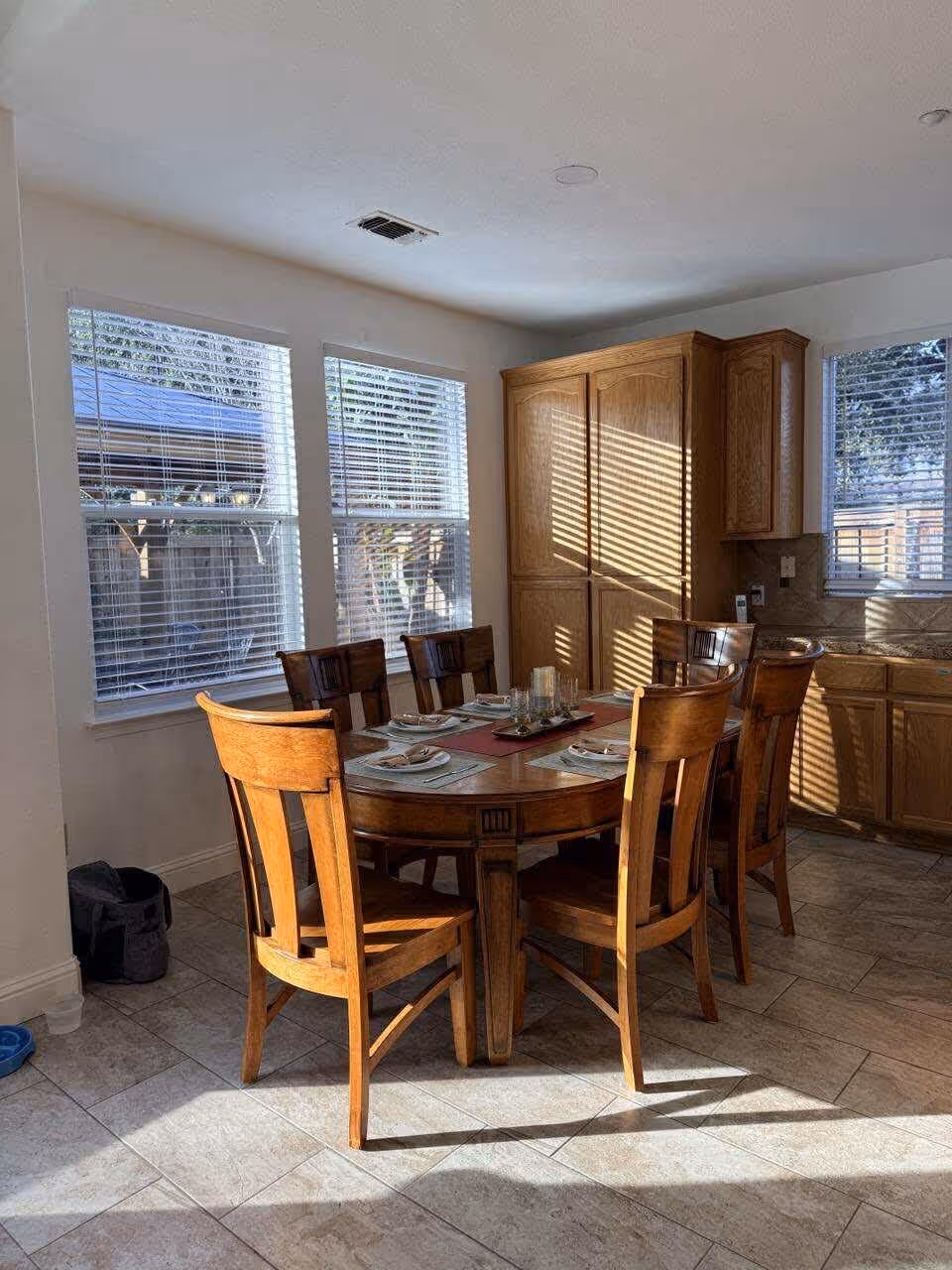 Wood dining table with six chairs set for a meal in a bright kitchen-dining area.