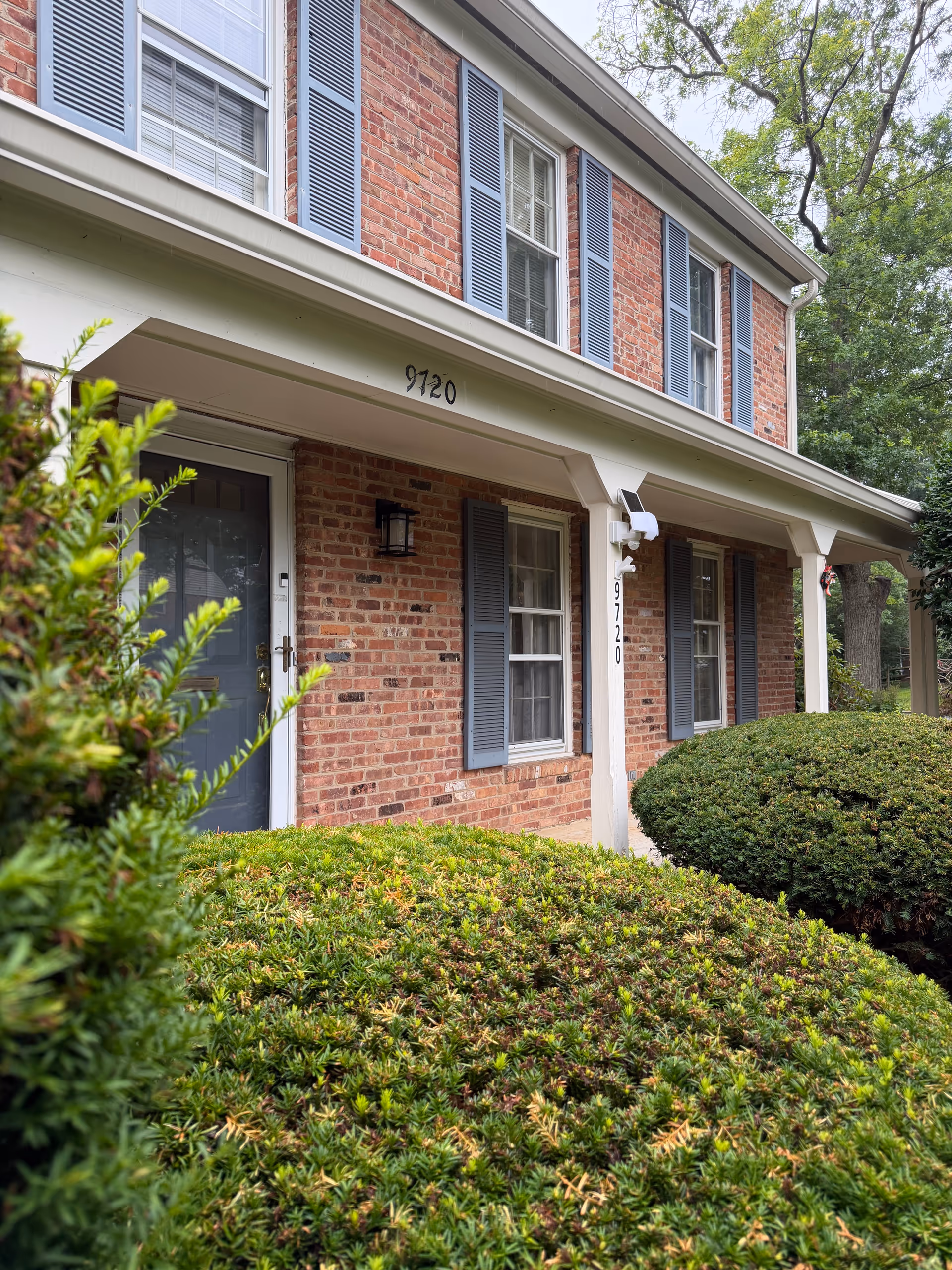 Brick senior living facility exterior with blue shutters and trimmed hedges.