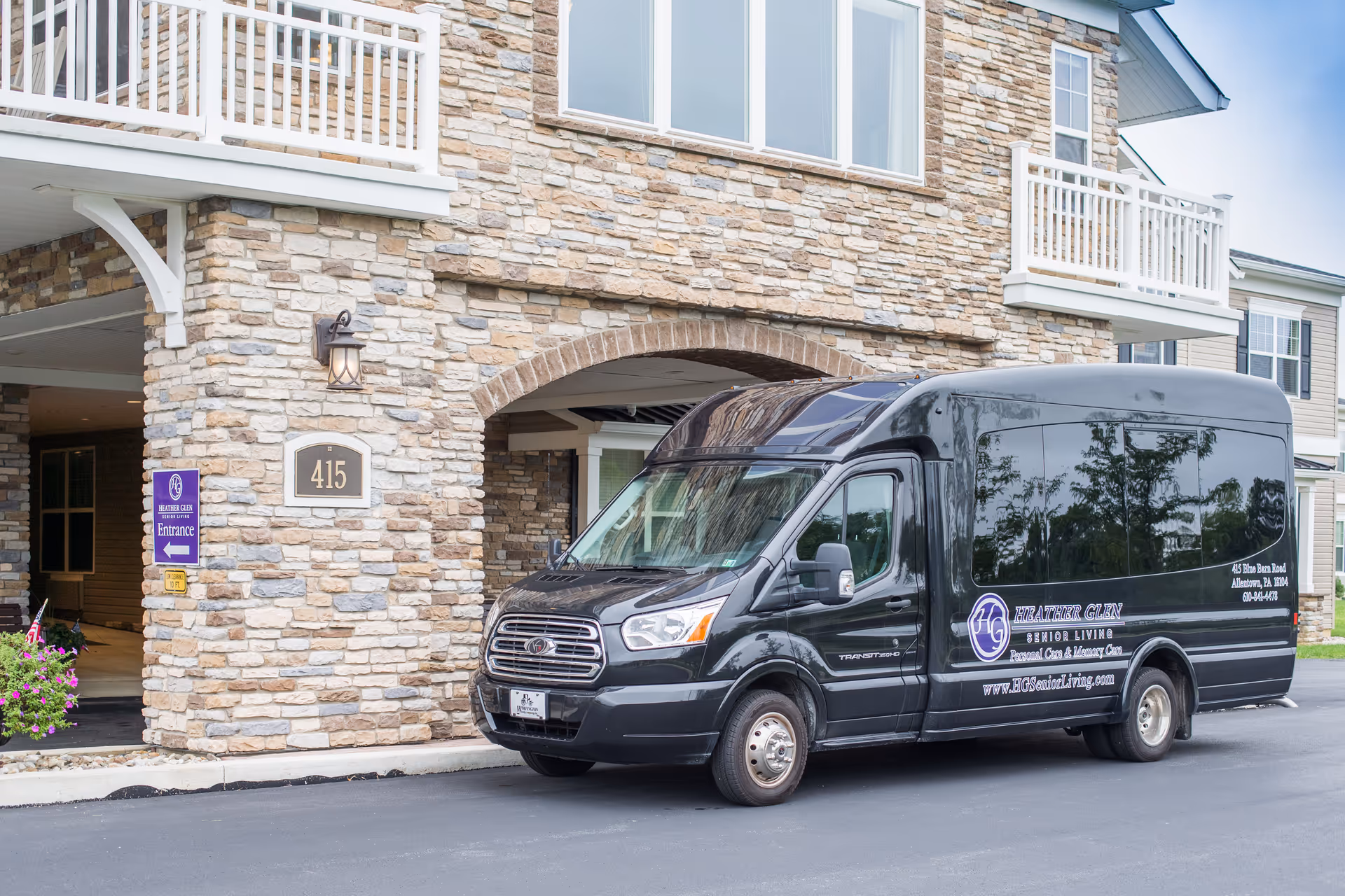 Stone-clad senior living building with a black shuttle van parked at the entrance