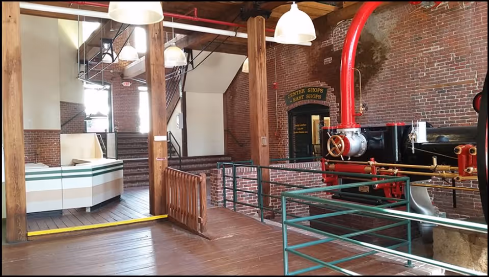 Industrial interior with brick walls, wooden beams, stairs, and large red equipment.
