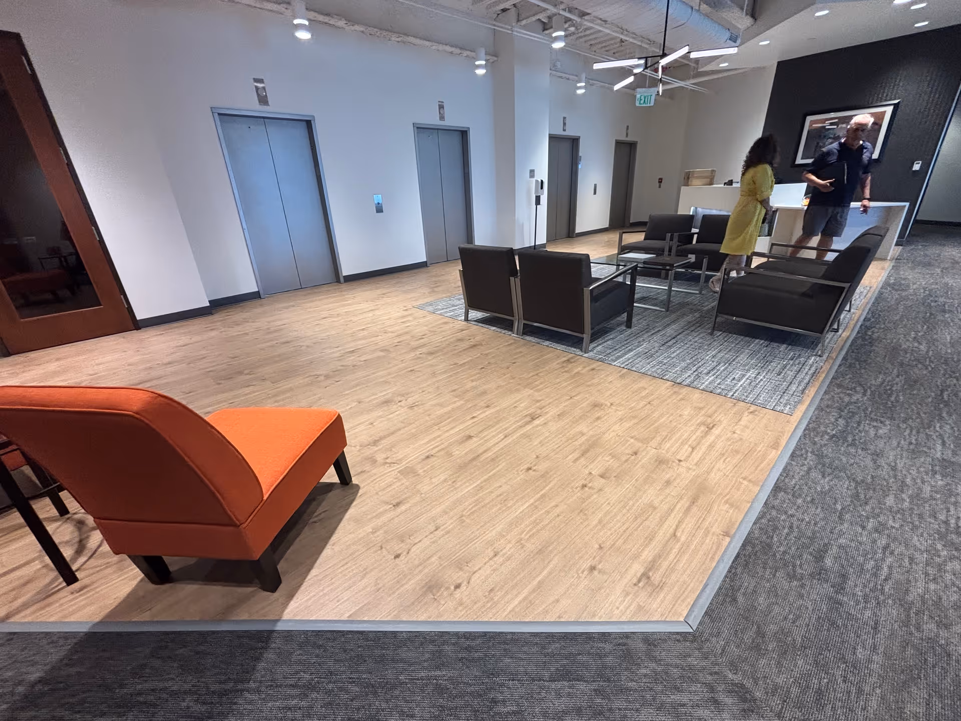 Modern senior living lounge with orange chaise, seating area, elevators, and reception.