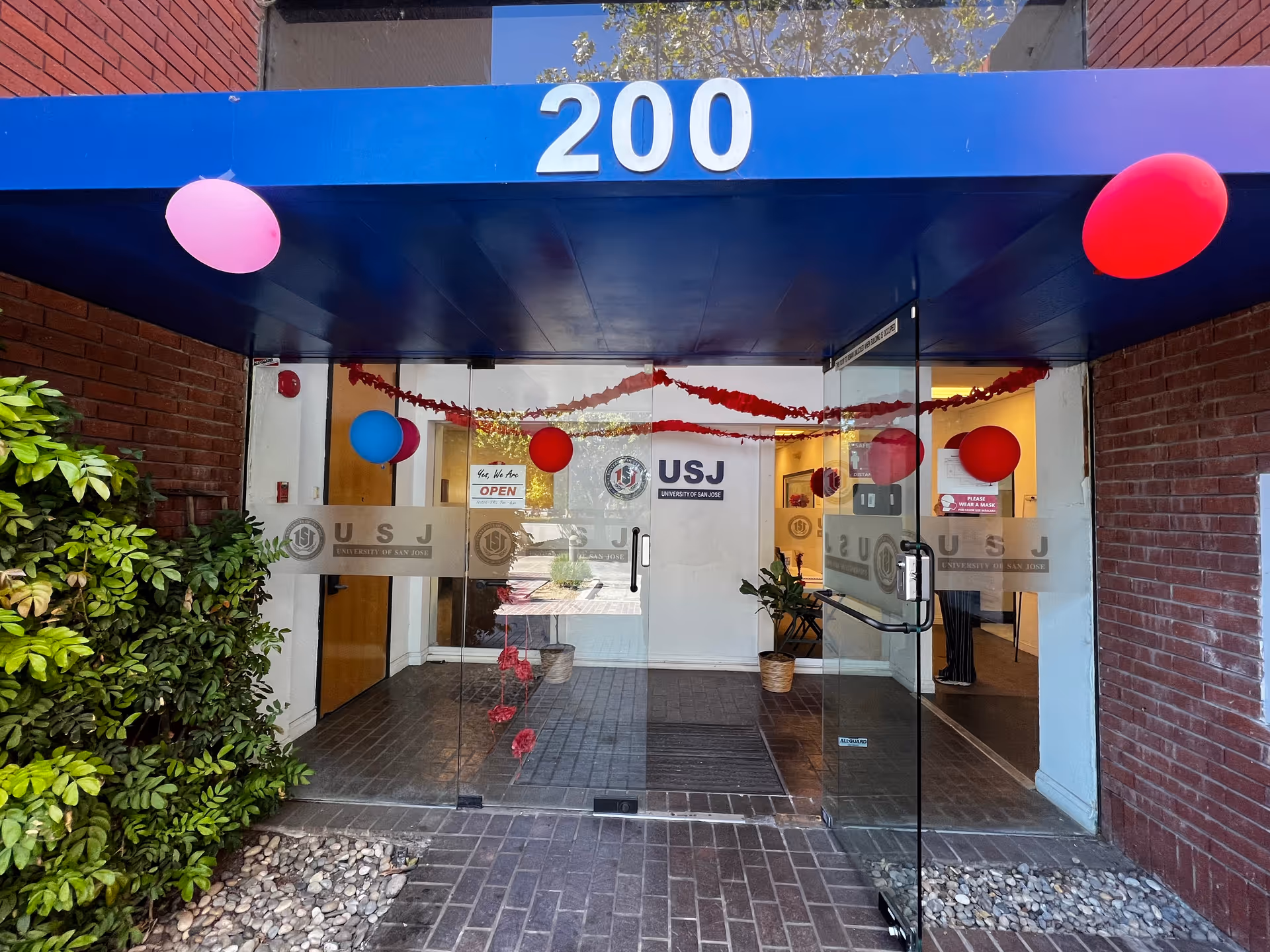 Glass entrance to University of San Jose (USJ) building with balloons and banners.