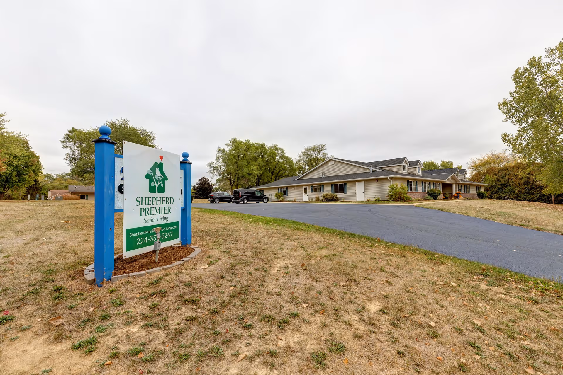 Front exterior of Shepherd Premier Senior Living with a blue-framed sign by the driveway.
