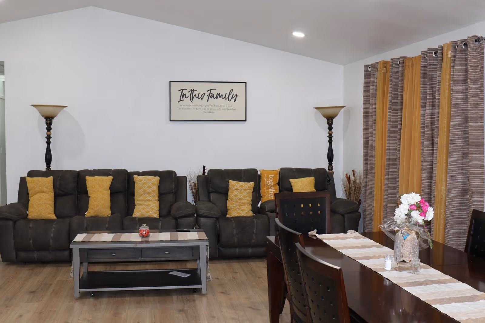 A cozy living room with dark sectional sofas, yellow cushions, and a dining table.
