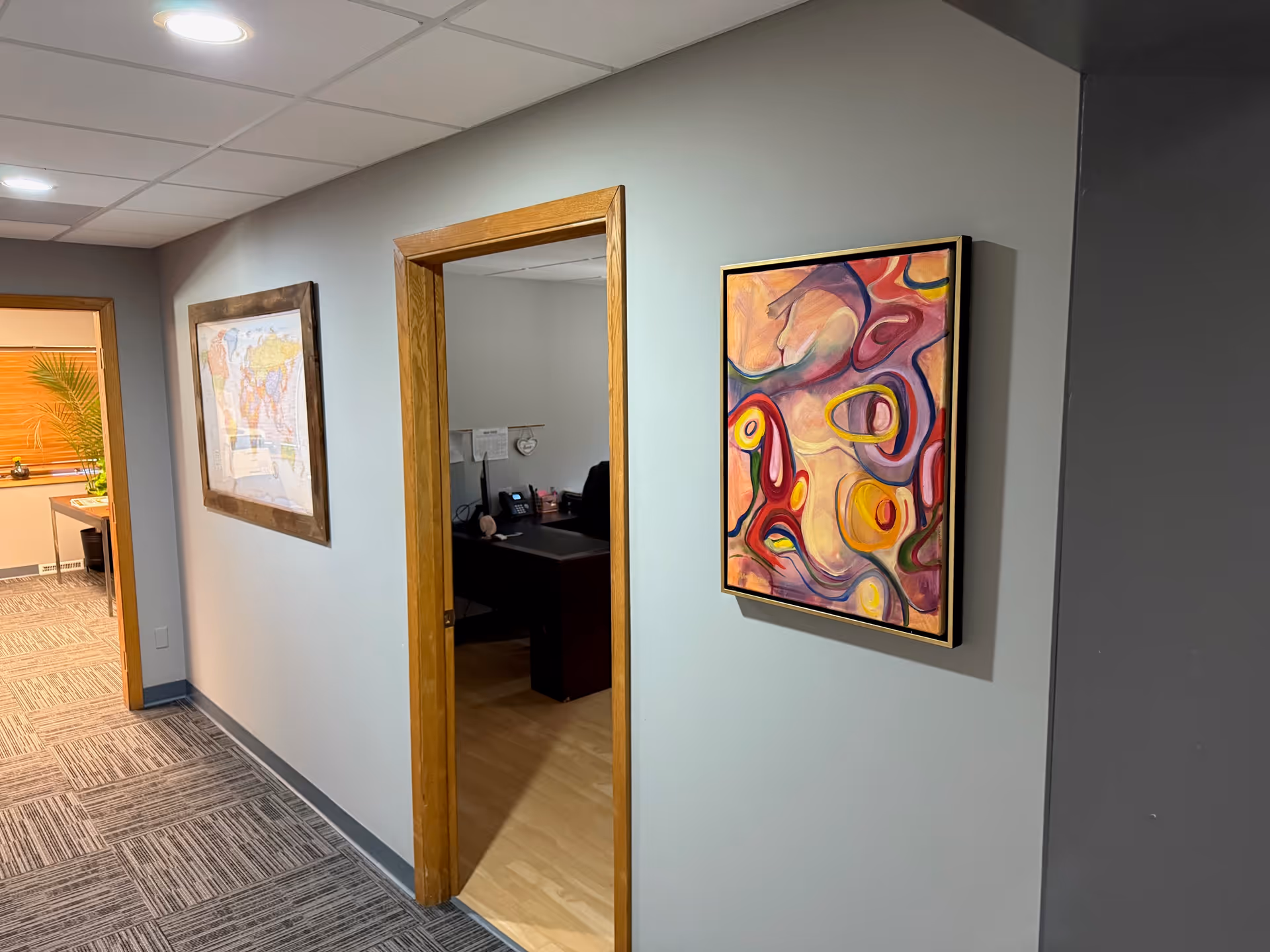 Interior hallway with framed art on walls and an open office doorway.