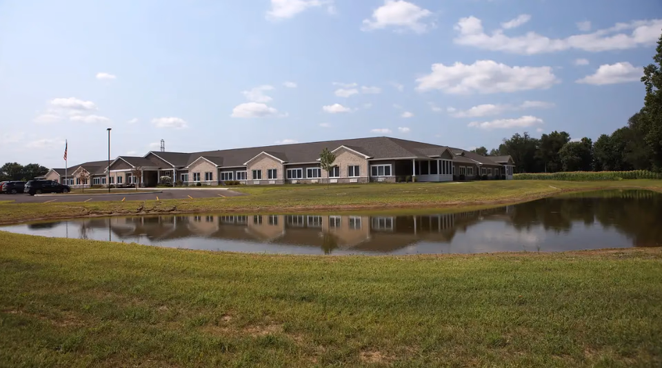 Front exterior of Autumn Trace Plymouth Assisted Living, showing parking and a pond.