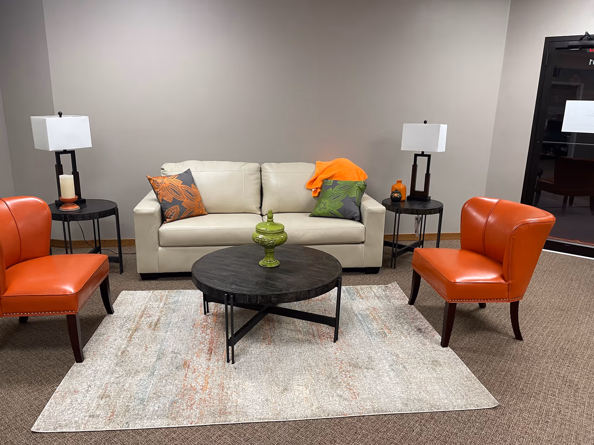Cozy senior living lounge with beige sofa, orange chairs, and two lamps.
