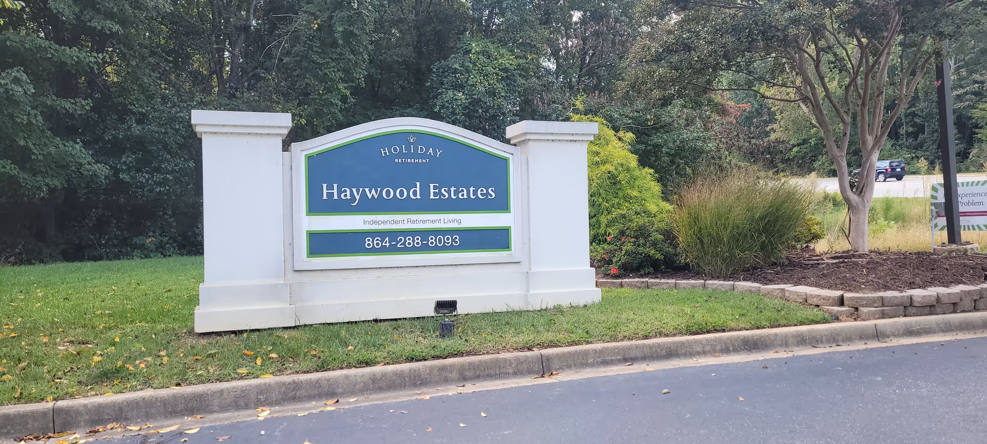 An outdoor sign for Haywood Estates sits on a grassy area with trees and a curb.