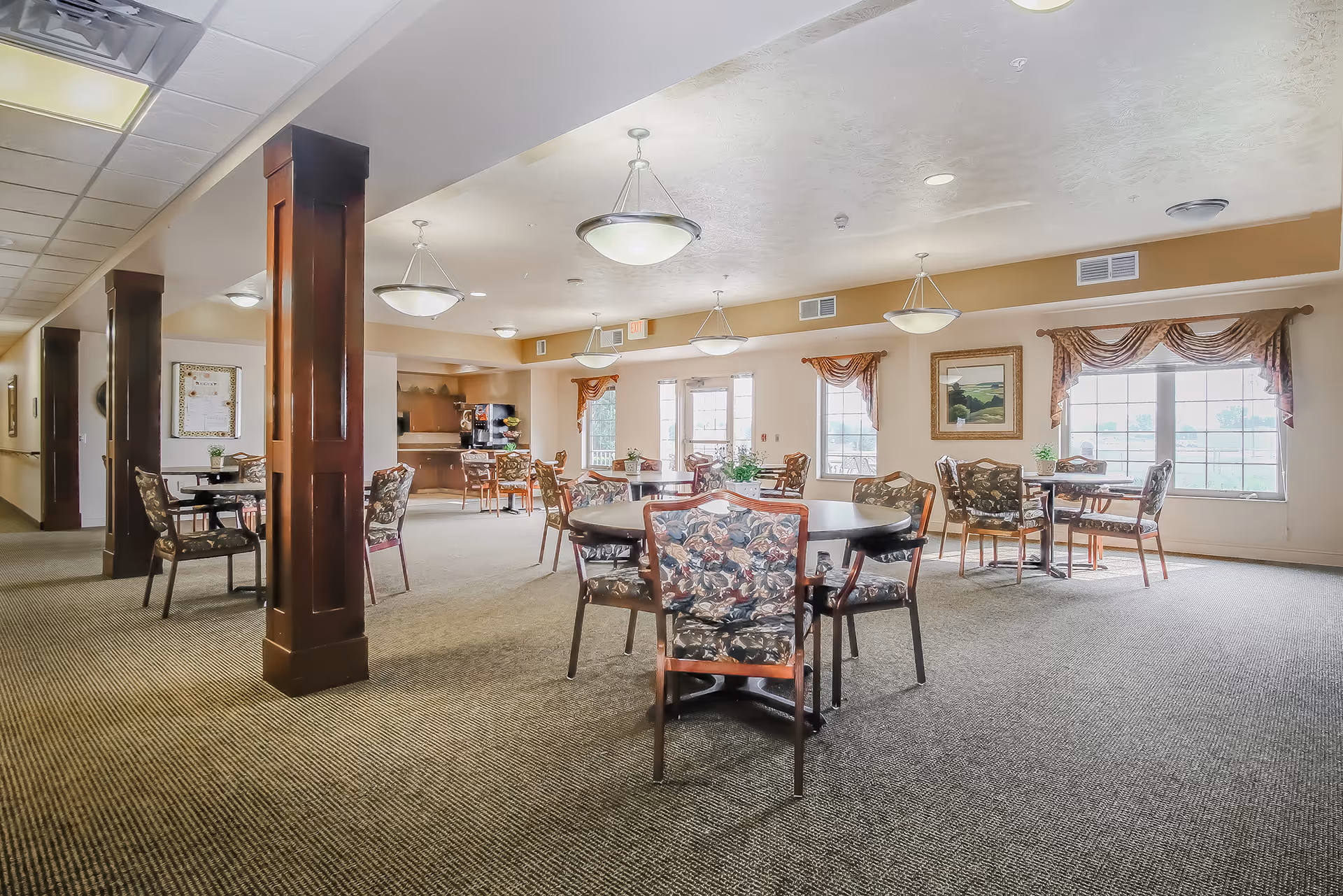 Large communal dining room with round tables and floral chairs in a senior facility.