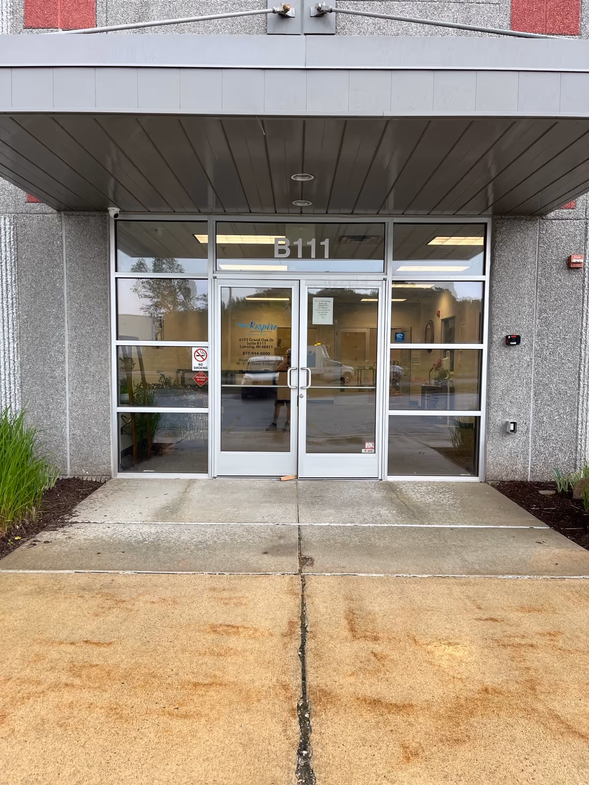 Glass double doors labeled B111 at a building entrance with a concrete sidewalk.
