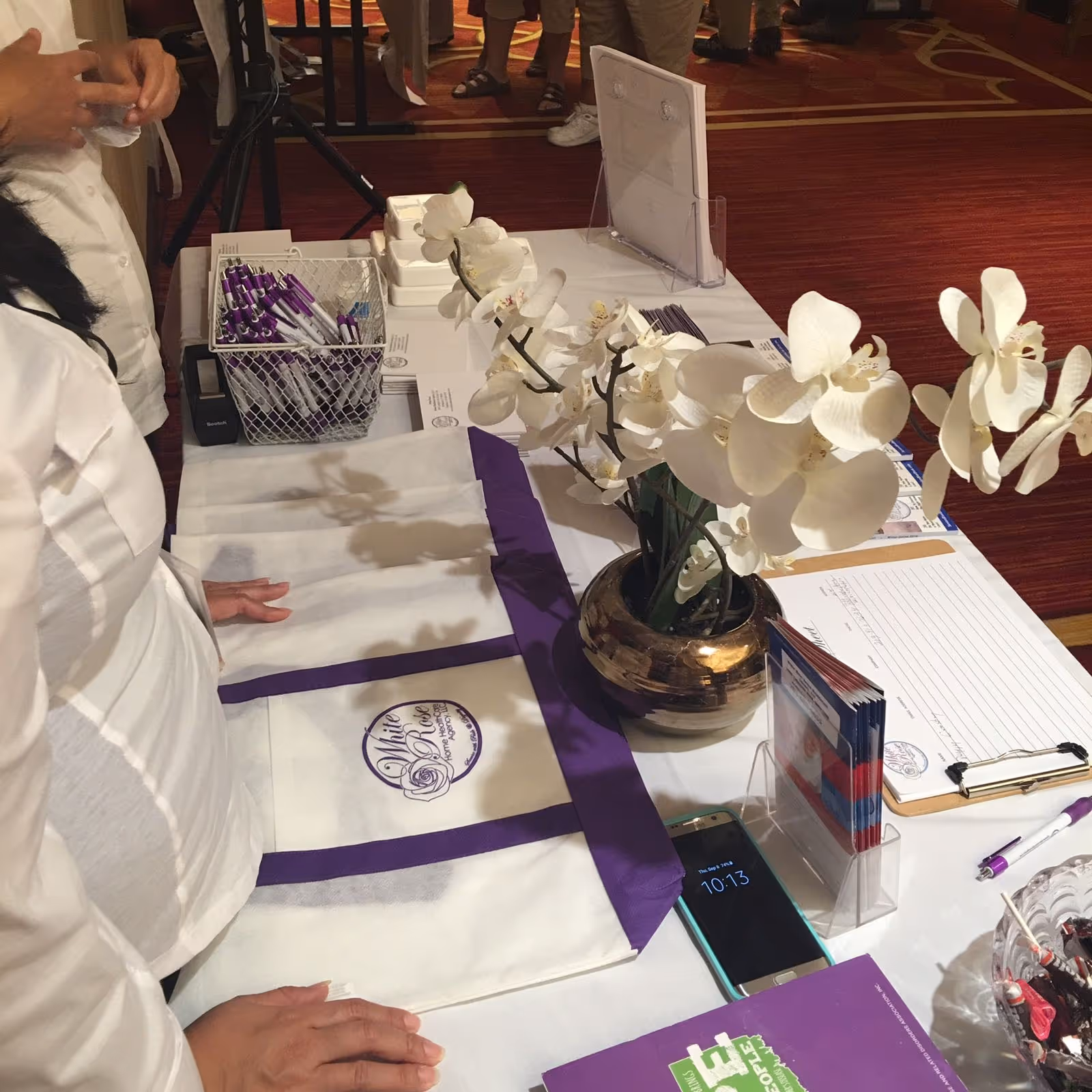 Reception table with orchid centerpiece, pens, forms, and staff at an indoor event