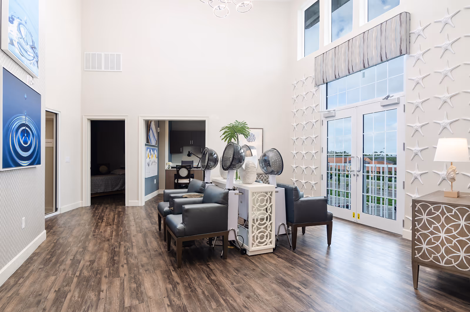 Bright, airy interior common room with salon hair-drying stations, seating, high windows and glass double doors to a balcony.