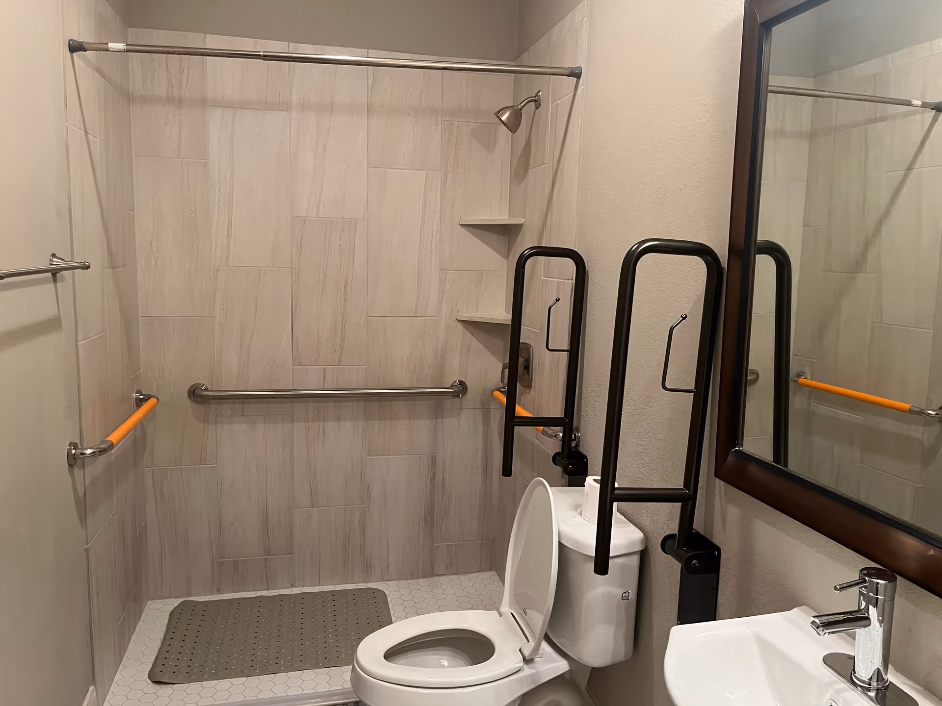 Accessible bathroom with grab bars, a toilet, sink, shower, and mirror.
