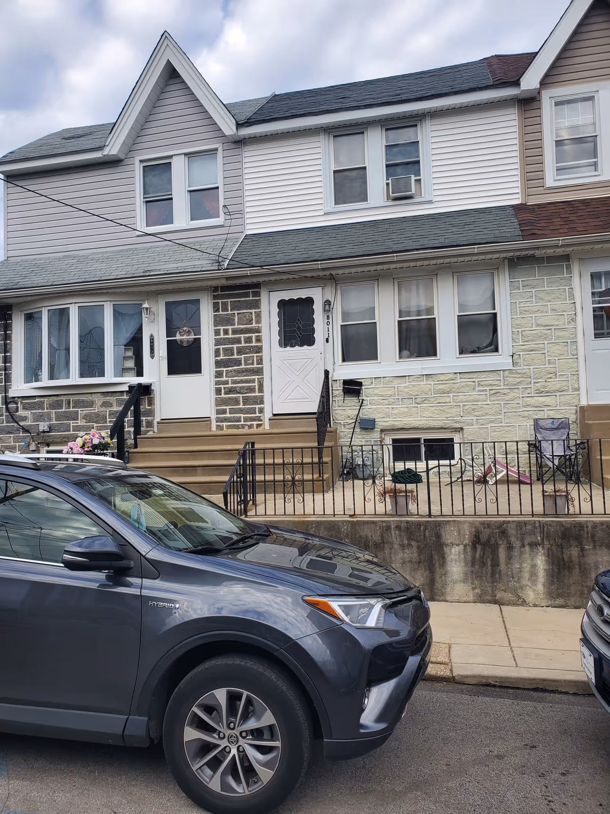 Front view of a two-story residential building with stairs, railings, and parked cars.