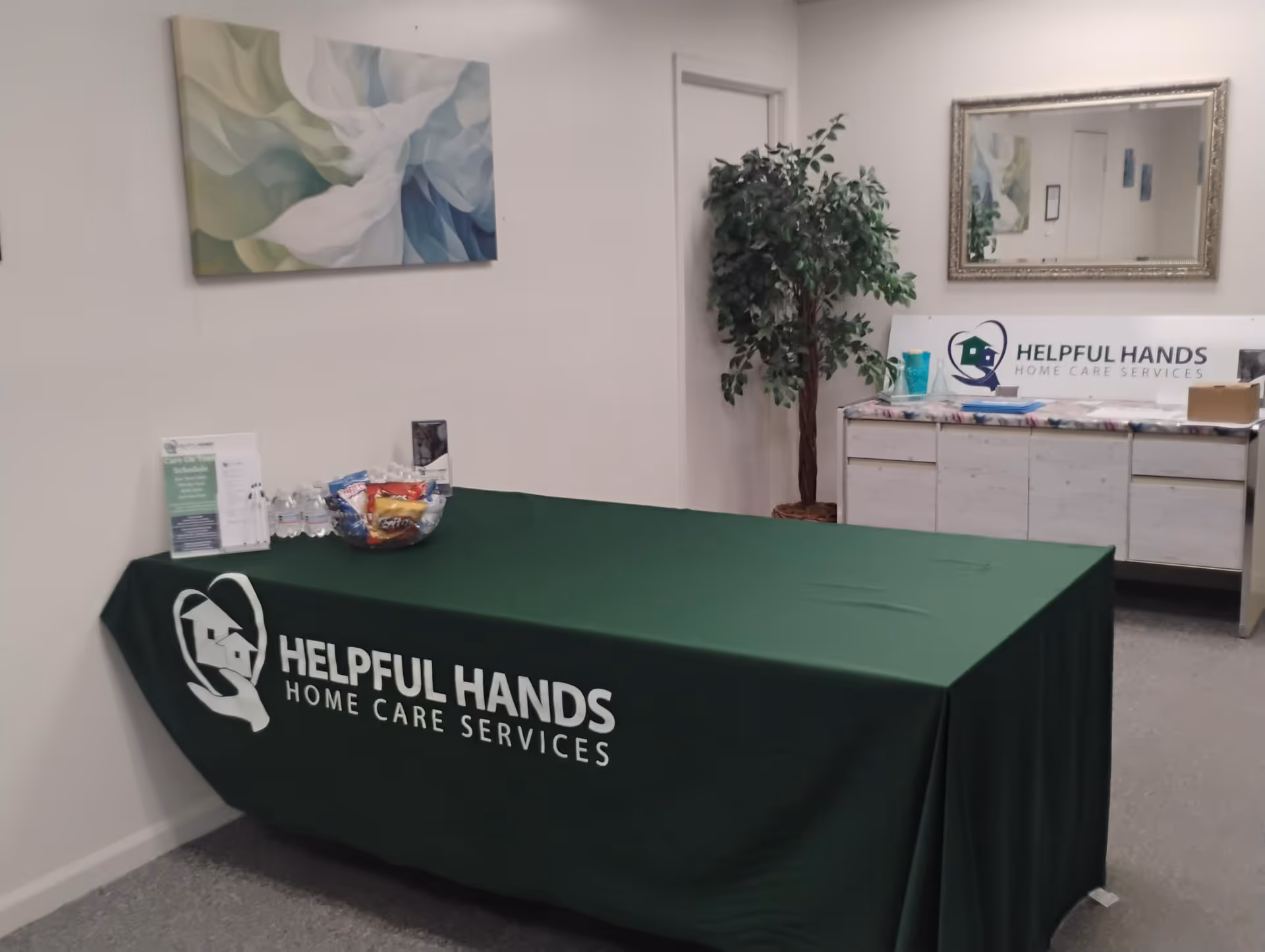 Lobby area featuring a green-draped reception table and branding for Helpful Hands Home Care Services