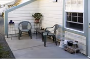 Outdoor concrete patio with two plastic chairs, a small table, and potted plant near the house.