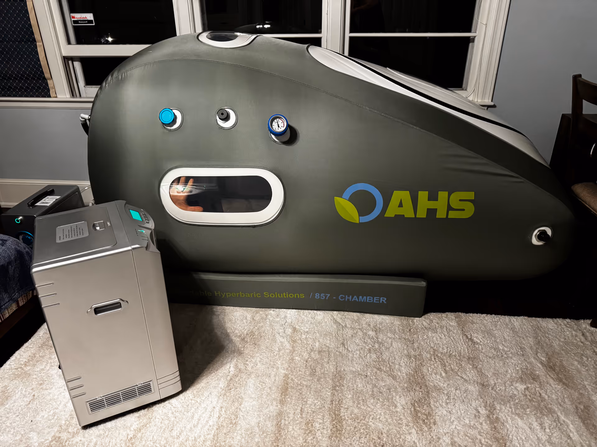 Indoor room with a large gray hyperbaric chamber labeled AHS and a nearby control unit.