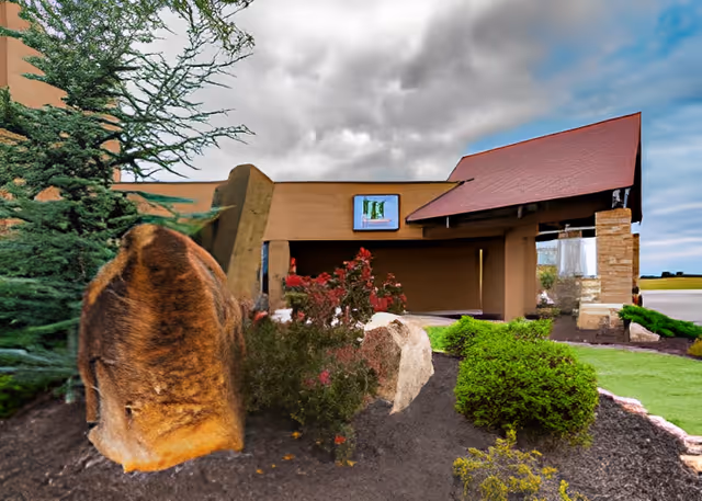 Front entrance of a senior living building with landscaped shrubs, large decorative rocks, and a red-roofed covered entry.