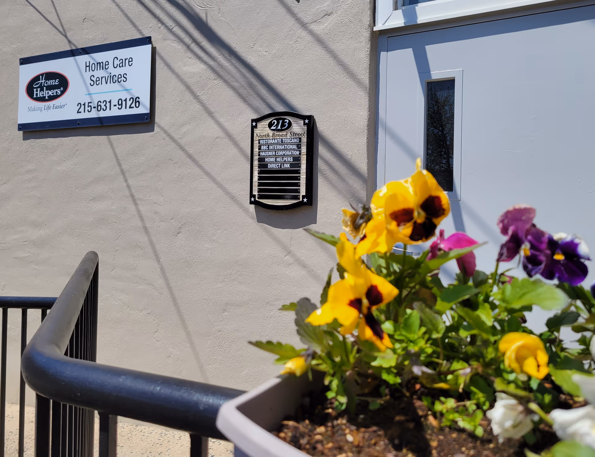 Exterior wall of a home care facility with signs and a flower planter.