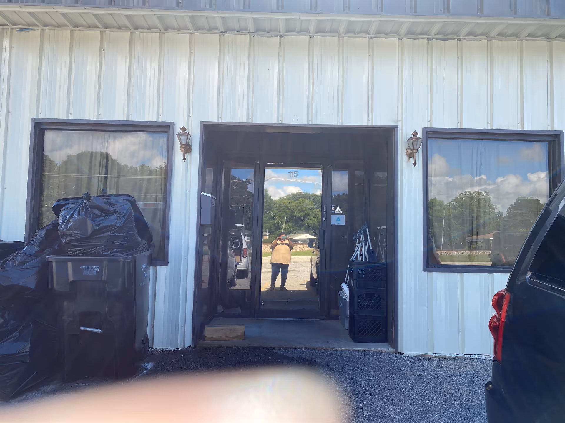 Front entrance of a light metal building with glass doors and trash bins.