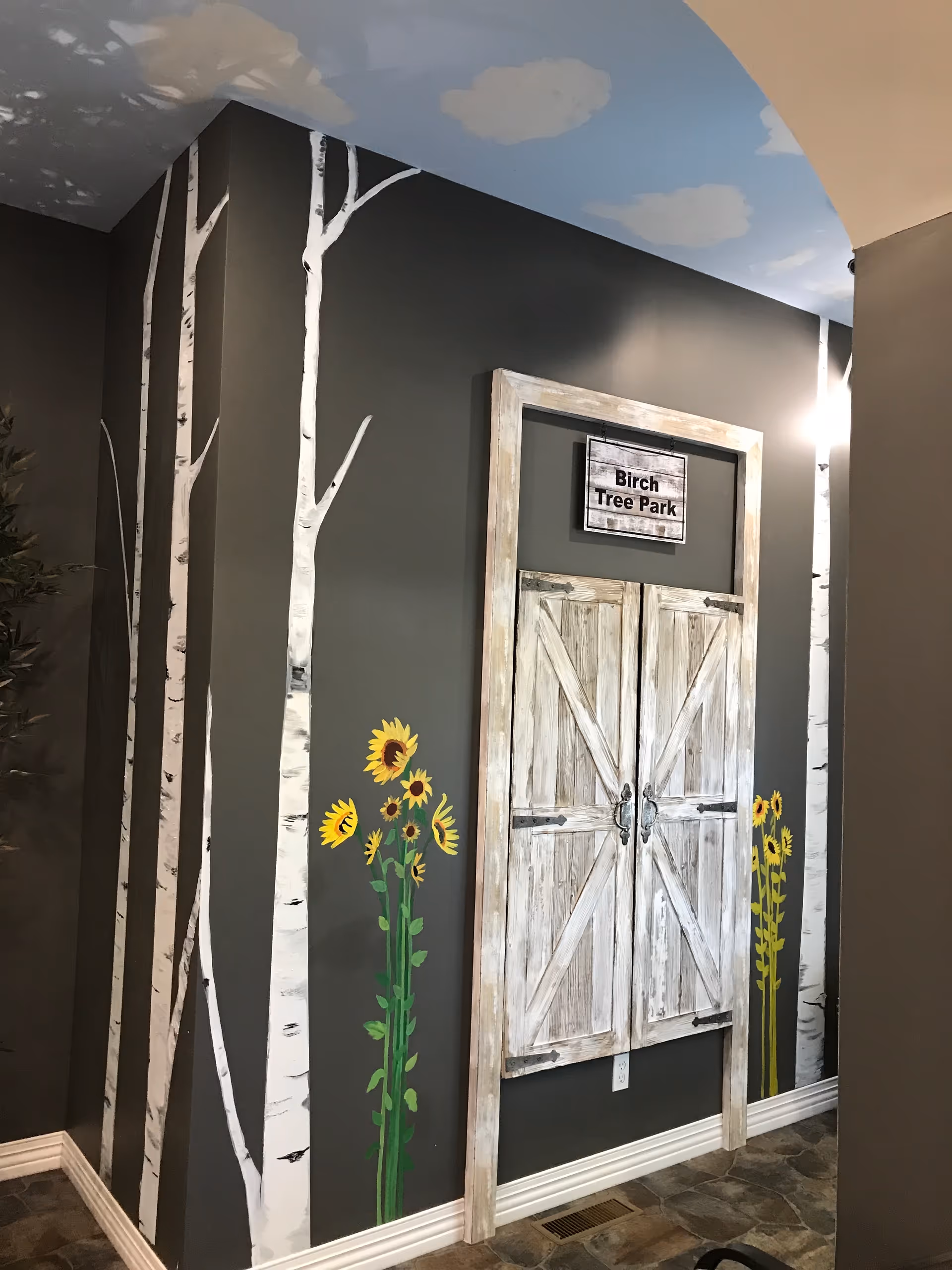 Indoor hallway with birch tree mural, rustic wooden door, sunflower decor.