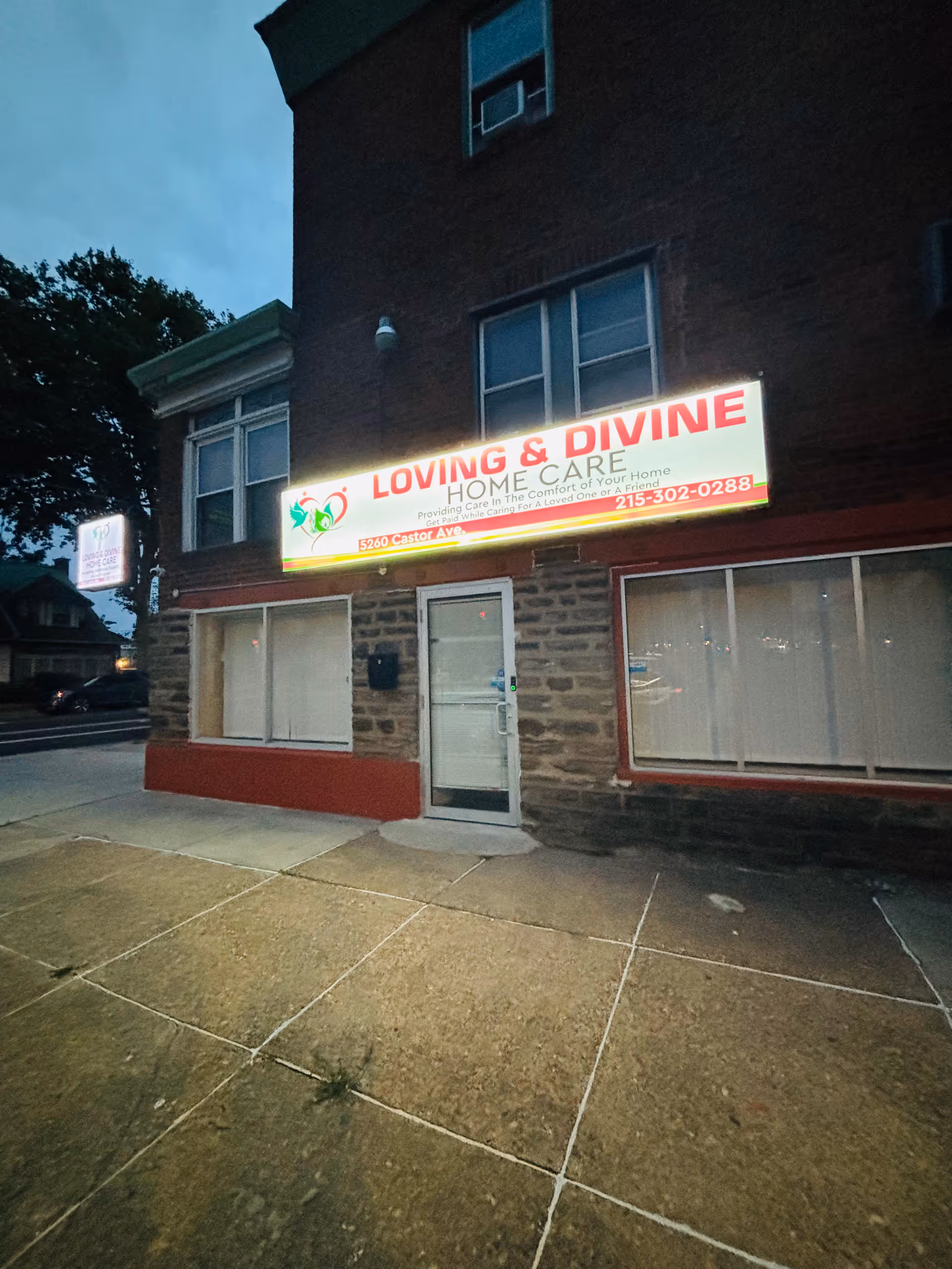 Brick storefront at dusk with a bright sign for Loving & Divine Home Care.