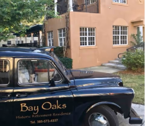 A vintage black car with Bay Oaks signage parked in front of a peach-colored retirement residence.