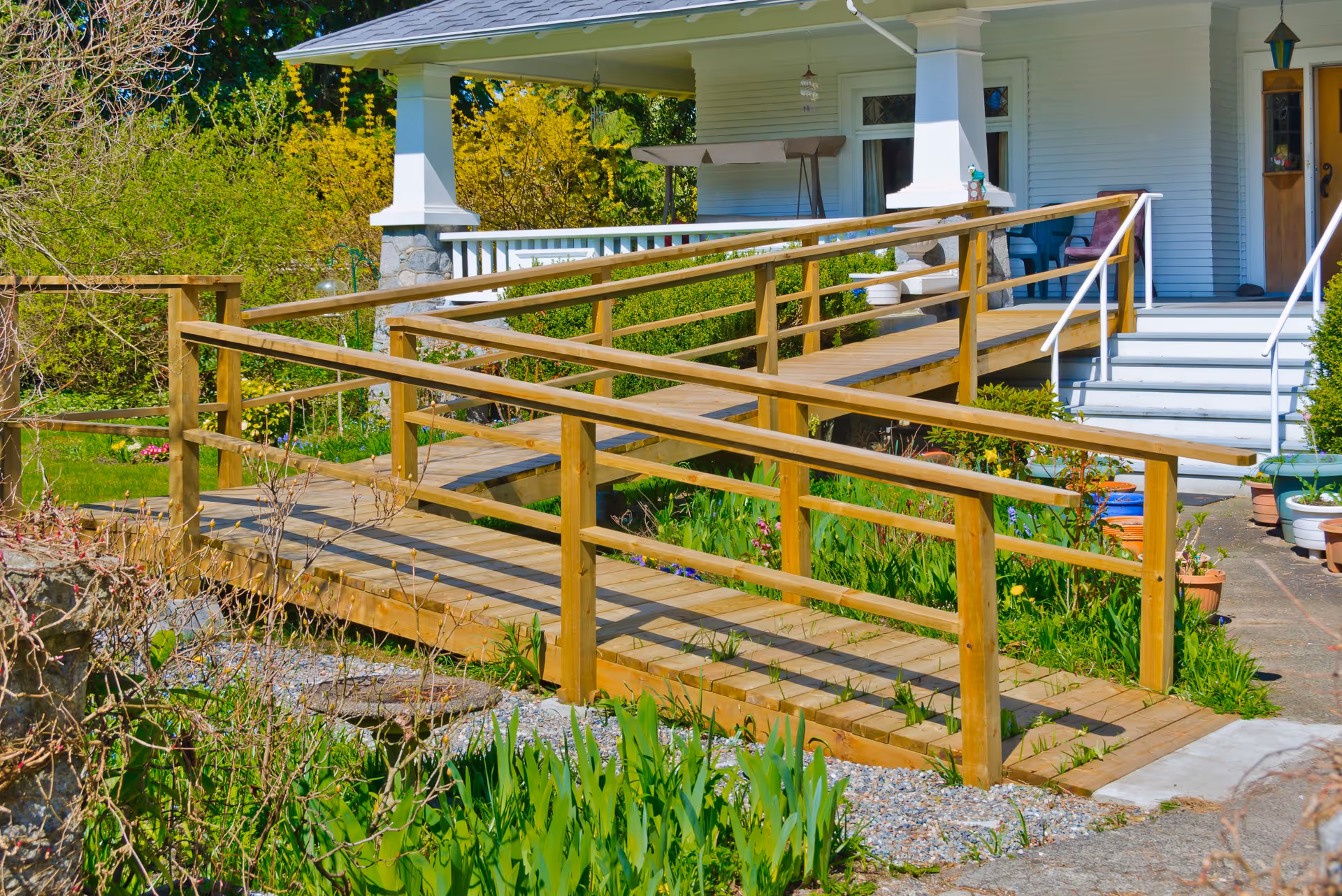 Wooden ramp with rails leads to a light-blue home entrance amid garden.