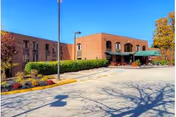 Front exterior of Green Meadows Nursing and Rehabilitation Center with brick facade and outdoor seating.