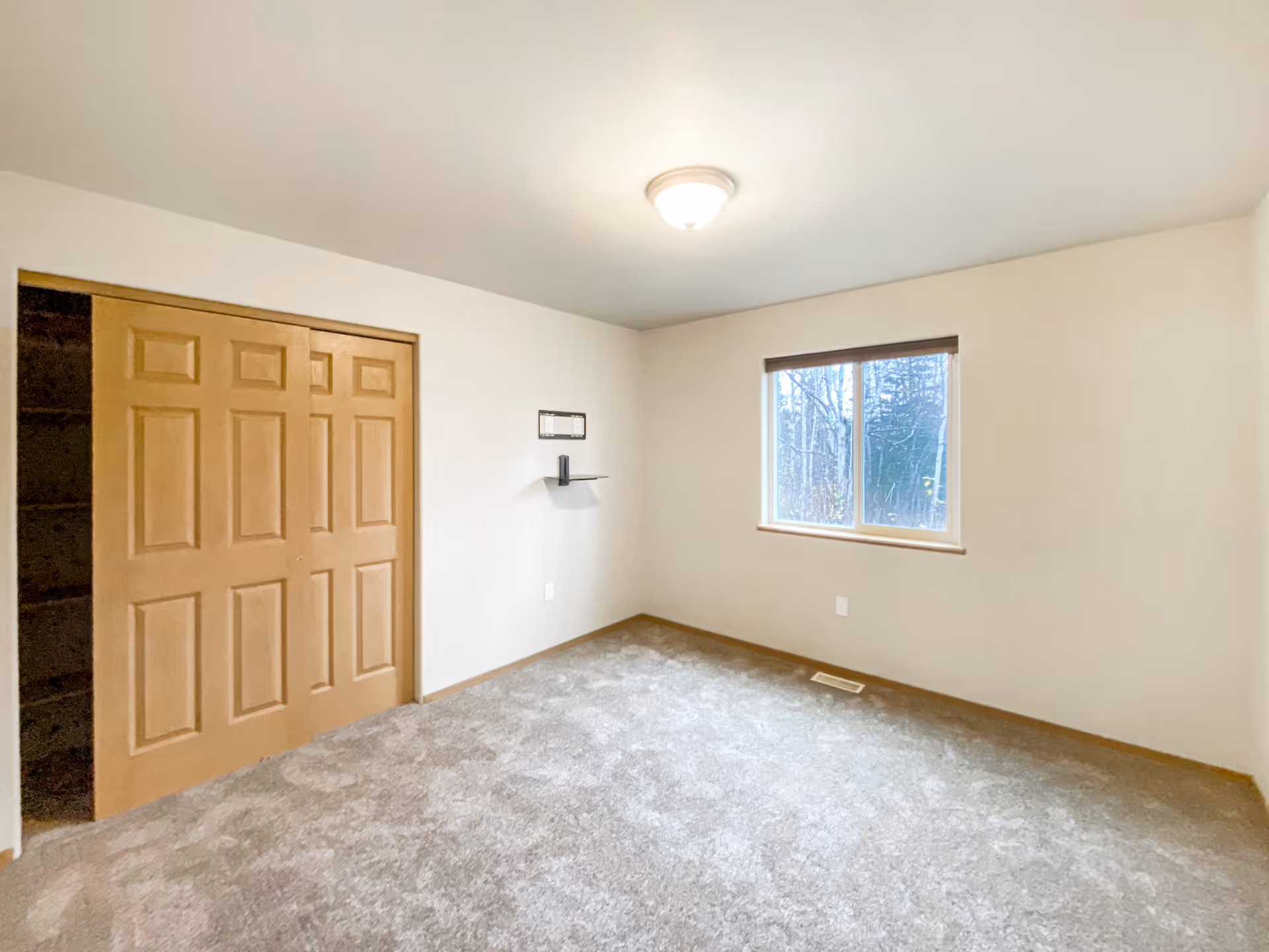 Empty bedroom with a wooden closet, window, and wall shelf in a senior facility.