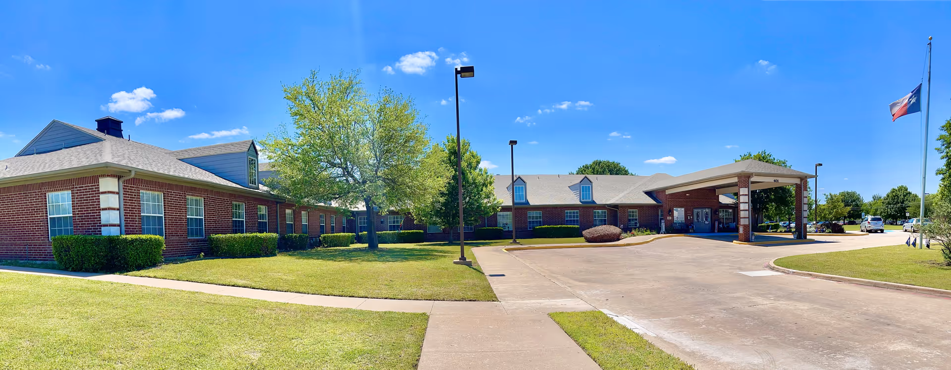 Wide view of Morada Waxahachie senior living facility exterior with entrance canopy and parking