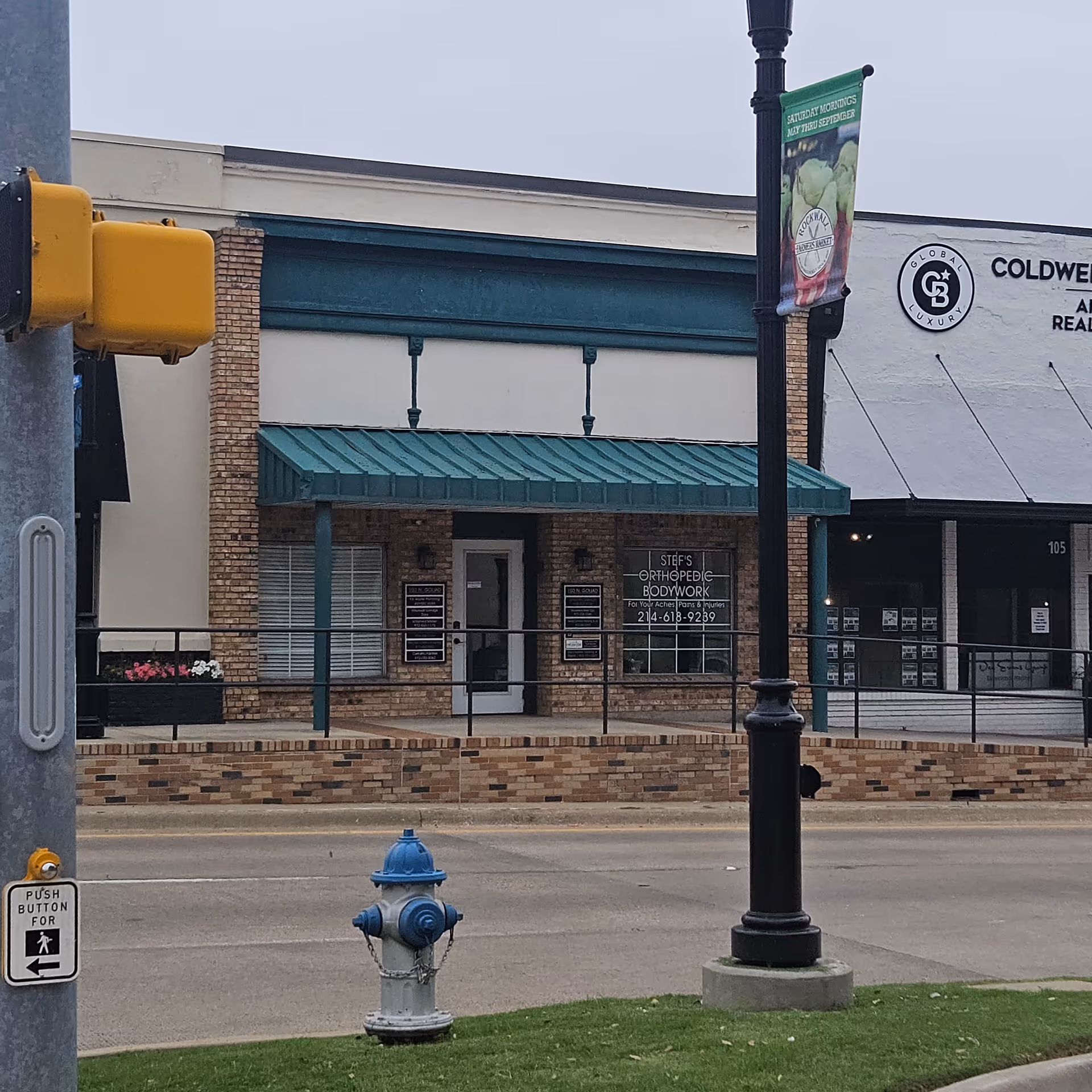 Street view of brick storefronts with a teal awning and sidewalks