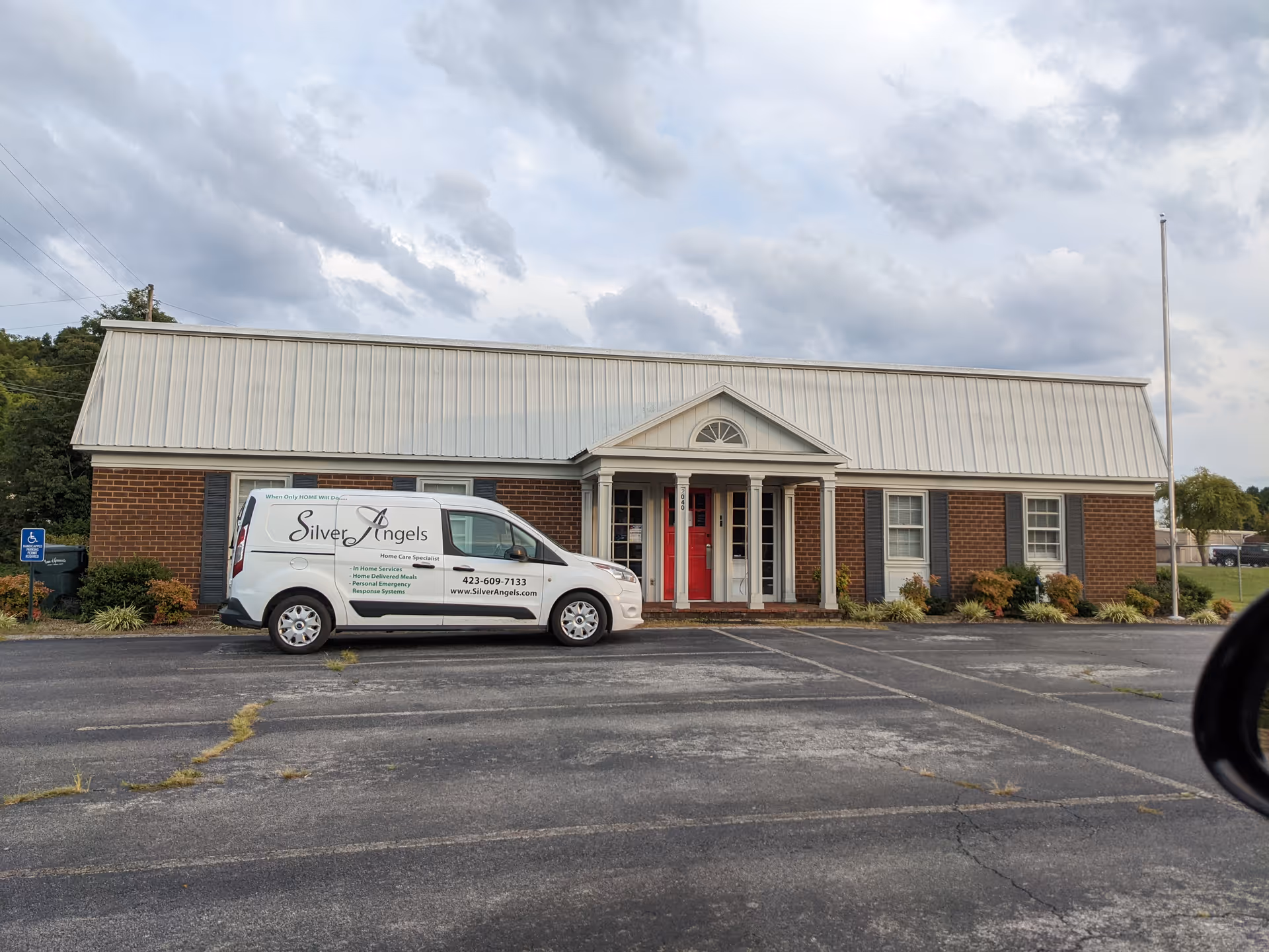 Brick senior living facility with a white metal roof and a Silver Angels van.