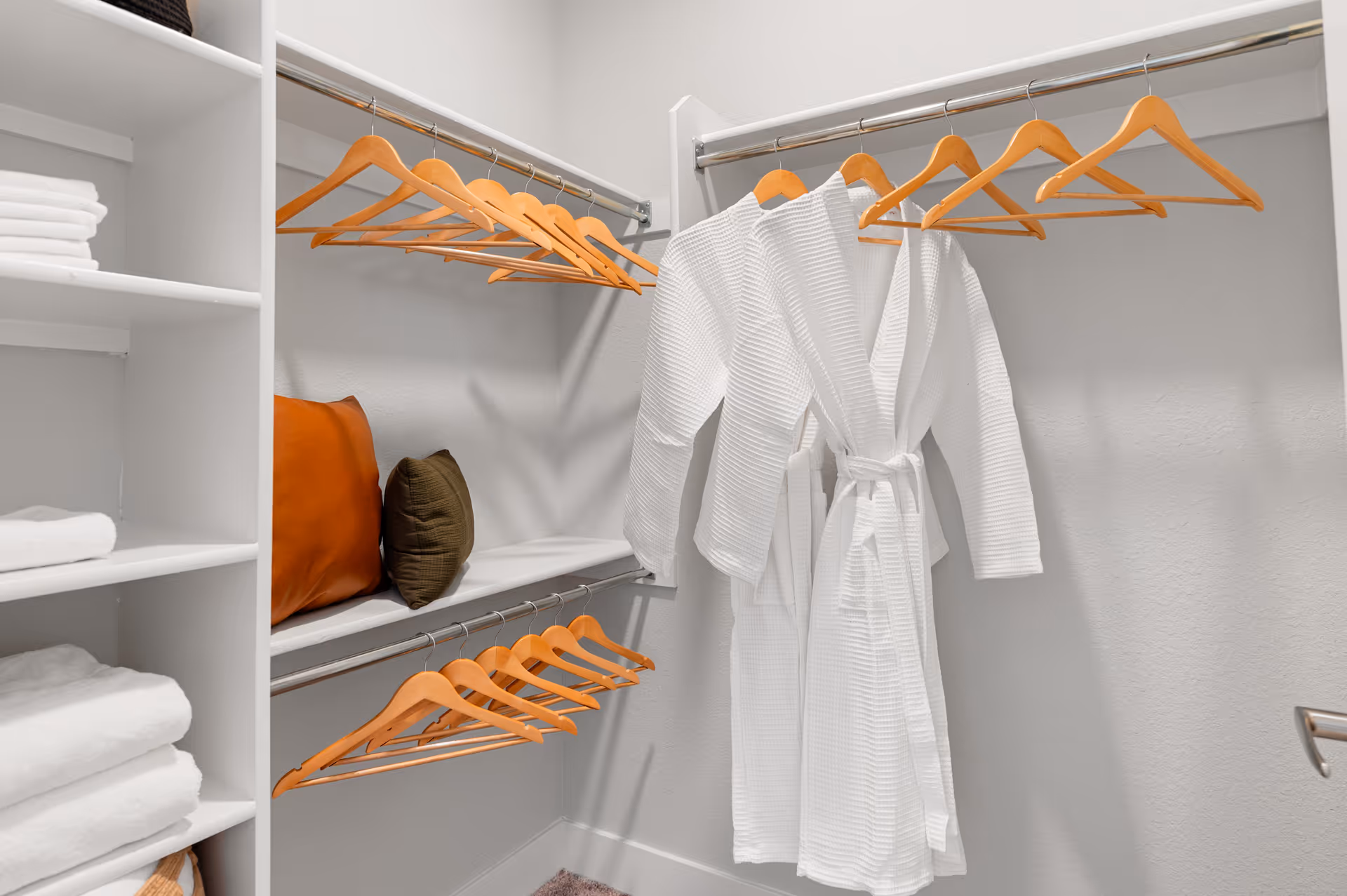 Walk-in closet with a white bathrobe on wooden hangers and towels on shelves.