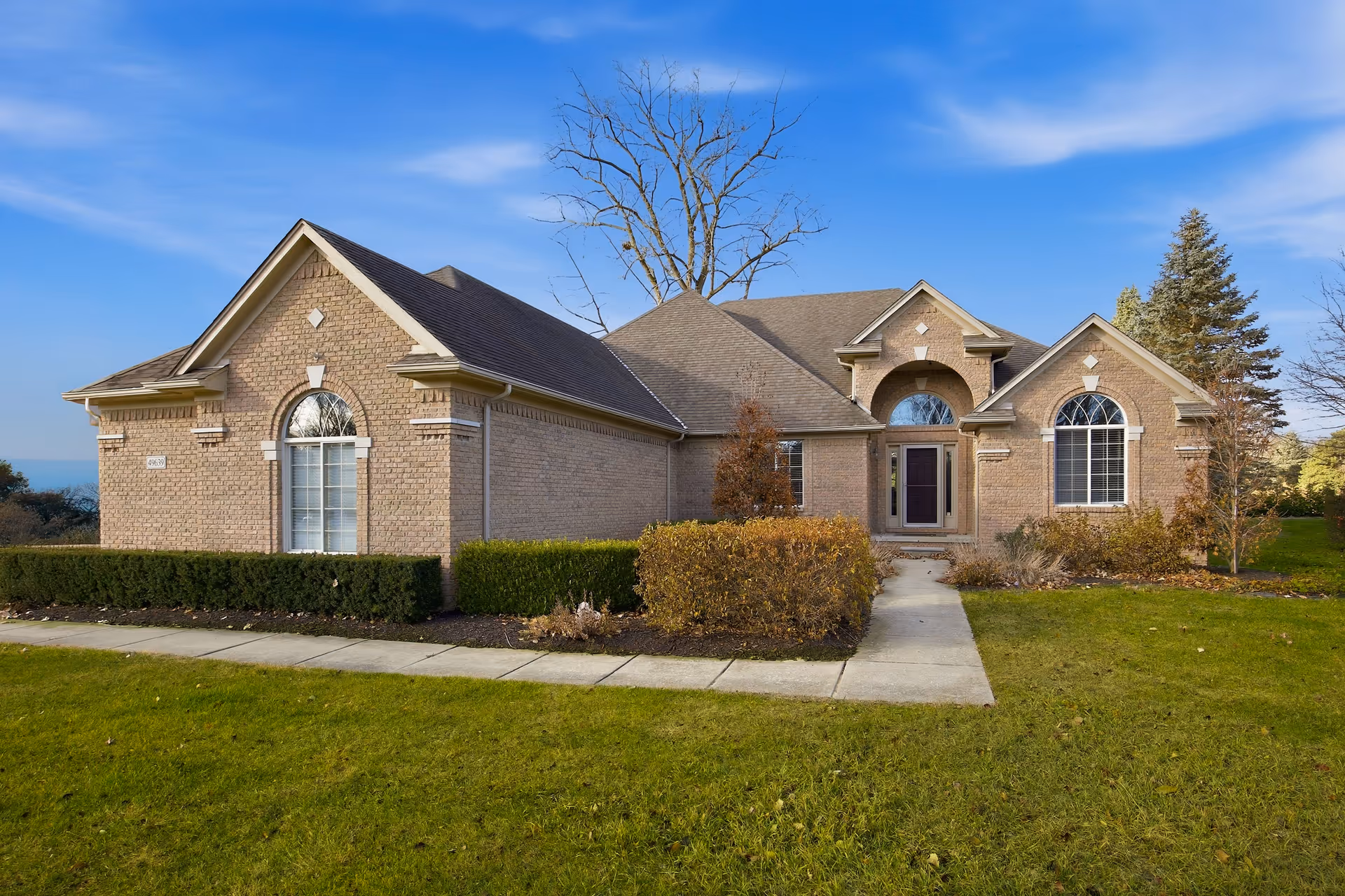 A brick senior living facility's front exterior with a curved entrance, well-kept lawn, and walkway.