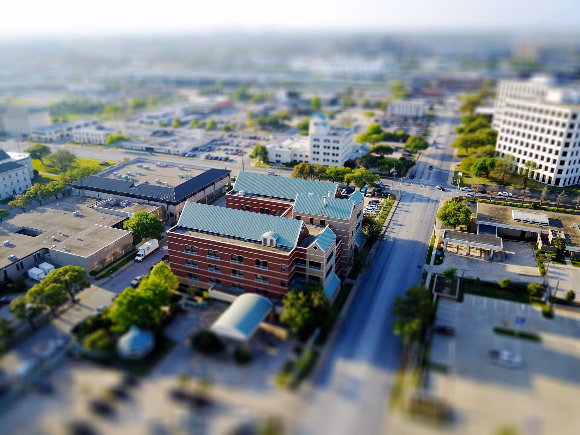 Aerial view of a red brick campus building with teal roof amid city blocks.