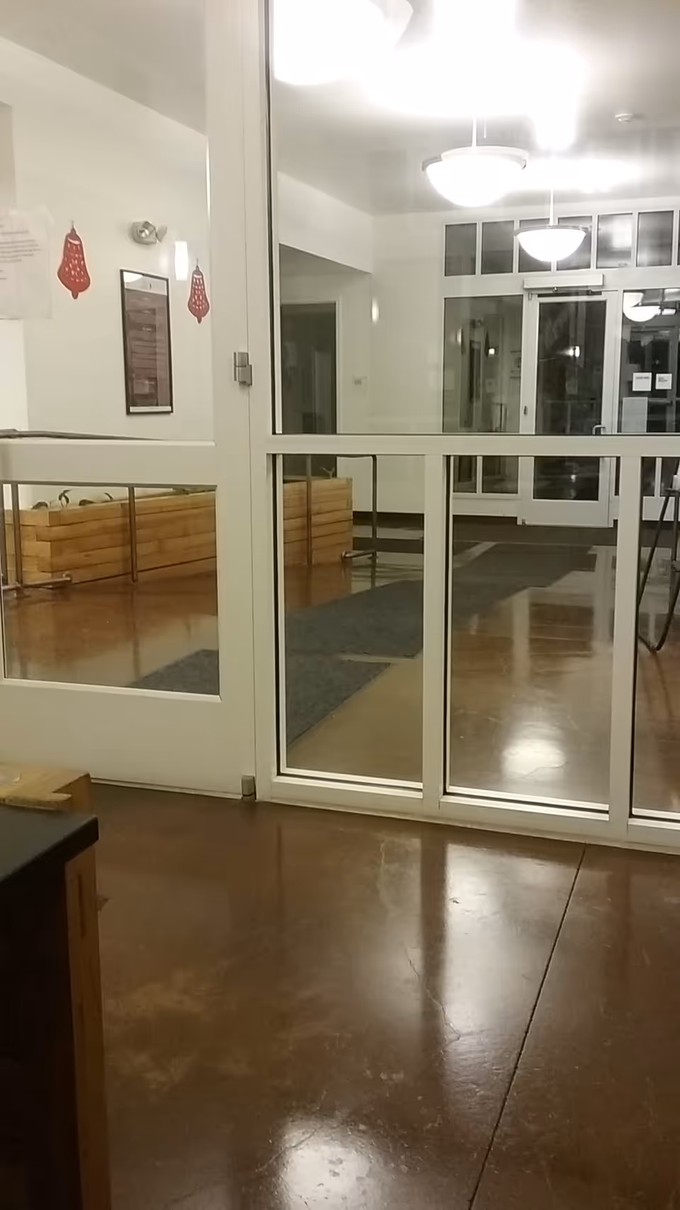 Interior lobby with glass doors, white walls, and glossy brown floor tiles.