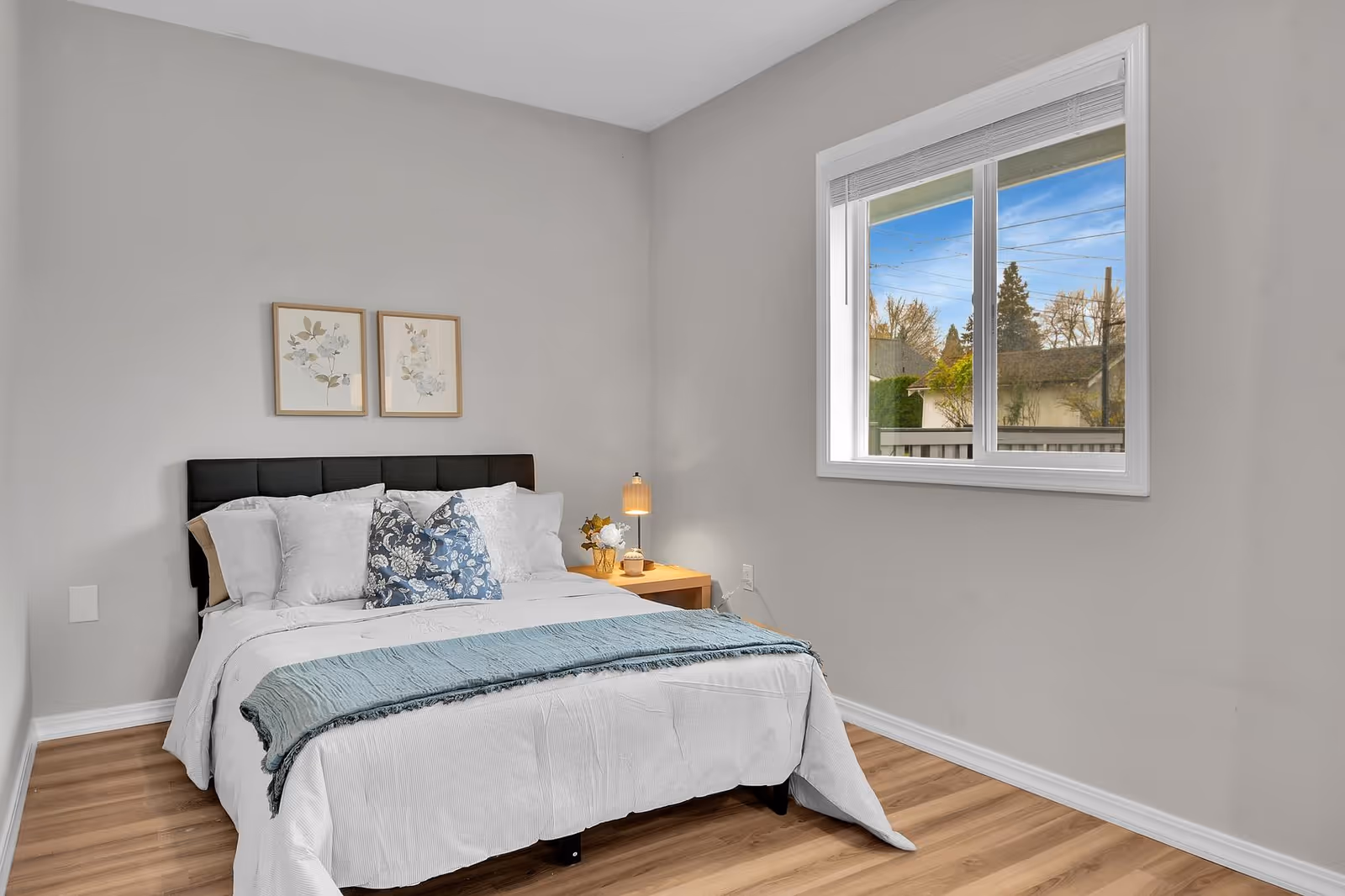 Neatly made bedroom with bed, nightstand, and window in a modern room.