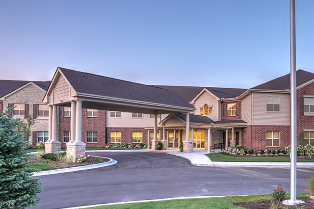Exterior view of a senior living facility entrance with porte-cochere and landscaped grounds.
