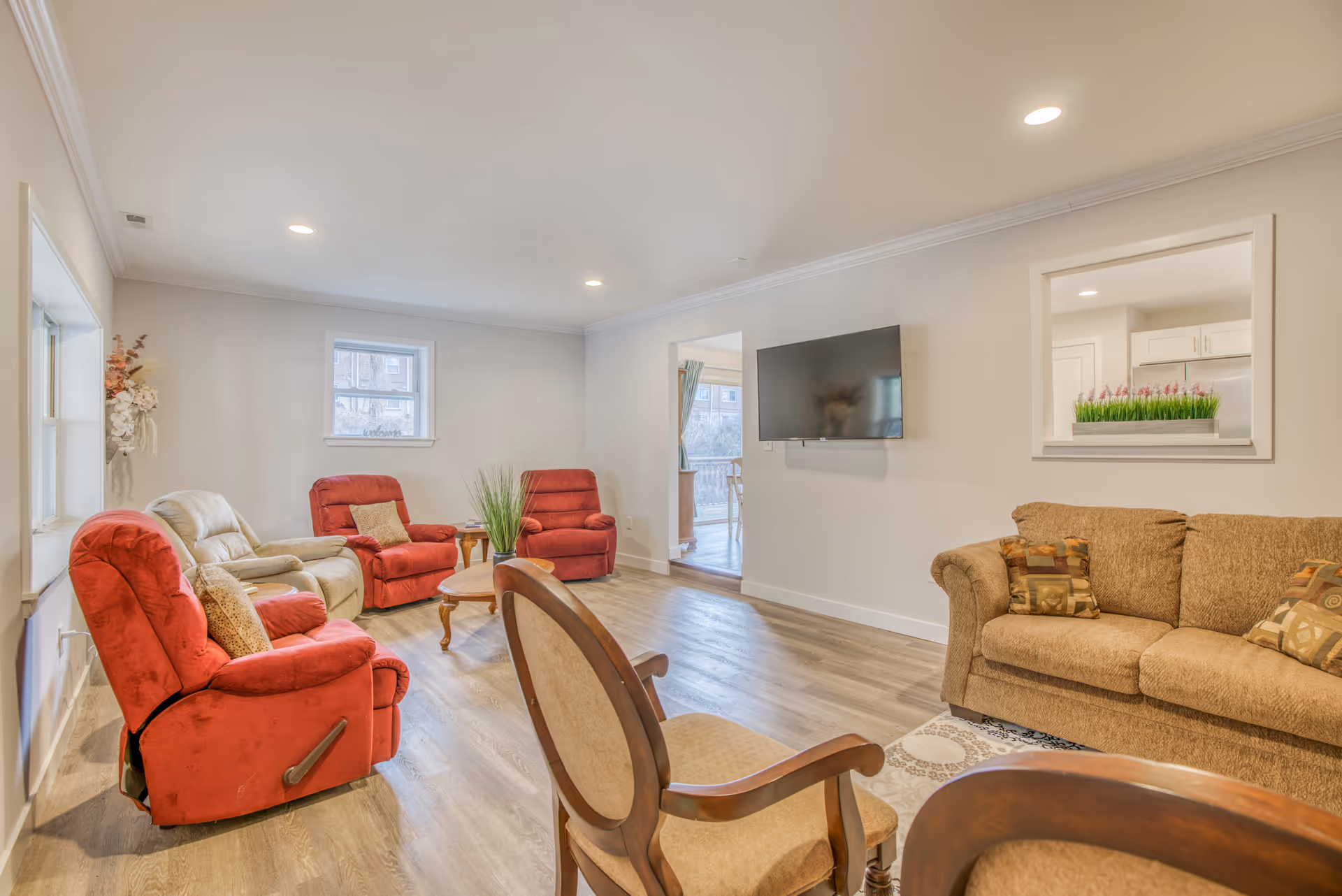 Bright senior living room with red recliners, tan sofa, coffee table, and wall TV.