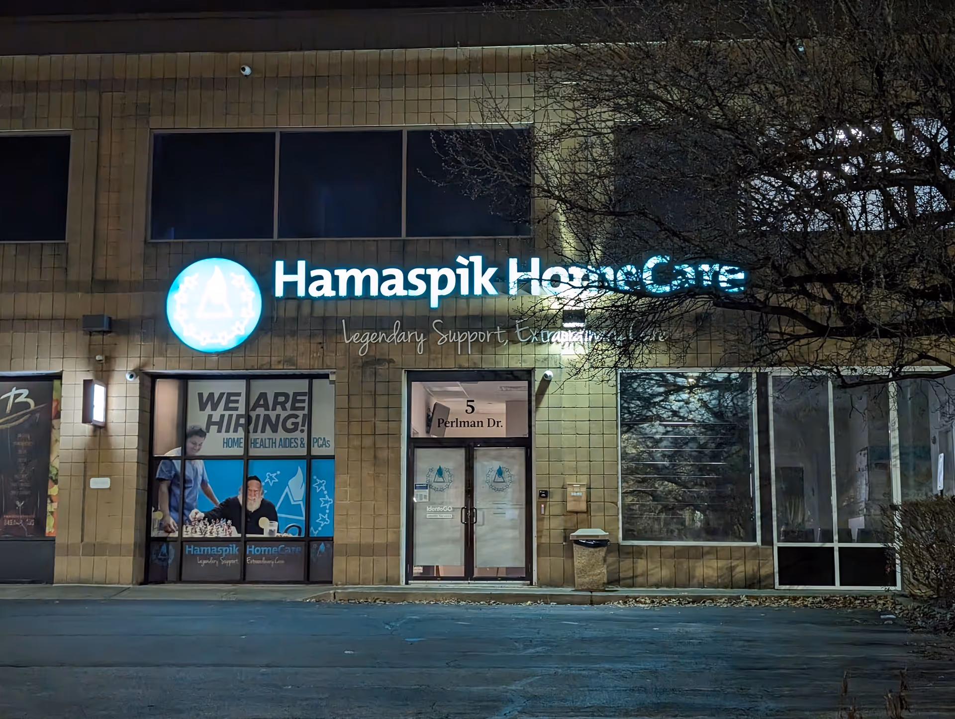 Nighttime exterior of Hamaspik HomeCare storefront with illuminated signage and We Are Hiring posters.