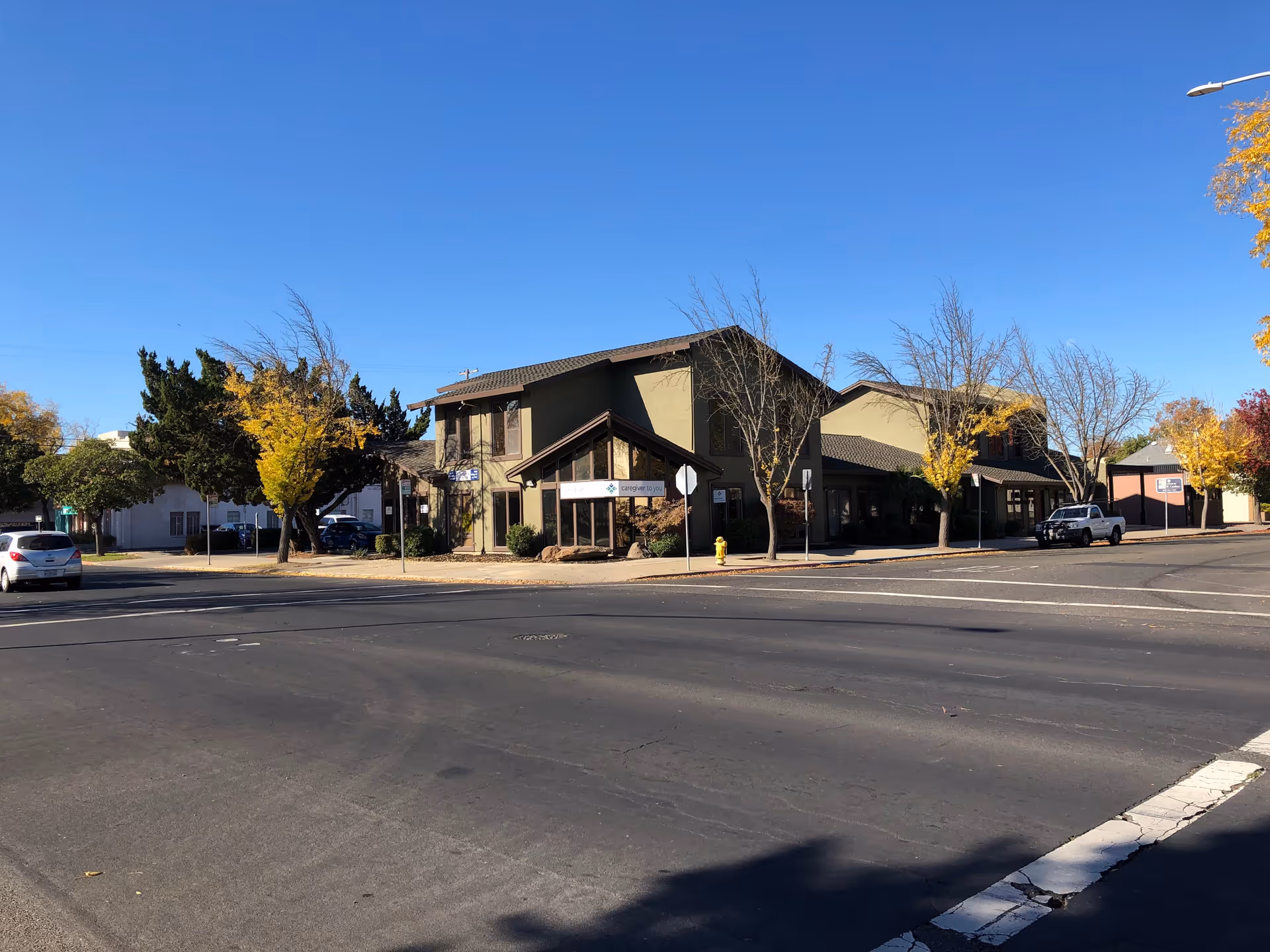 Exterior view of Caregiver To You facility along a street with trees and parked cars.