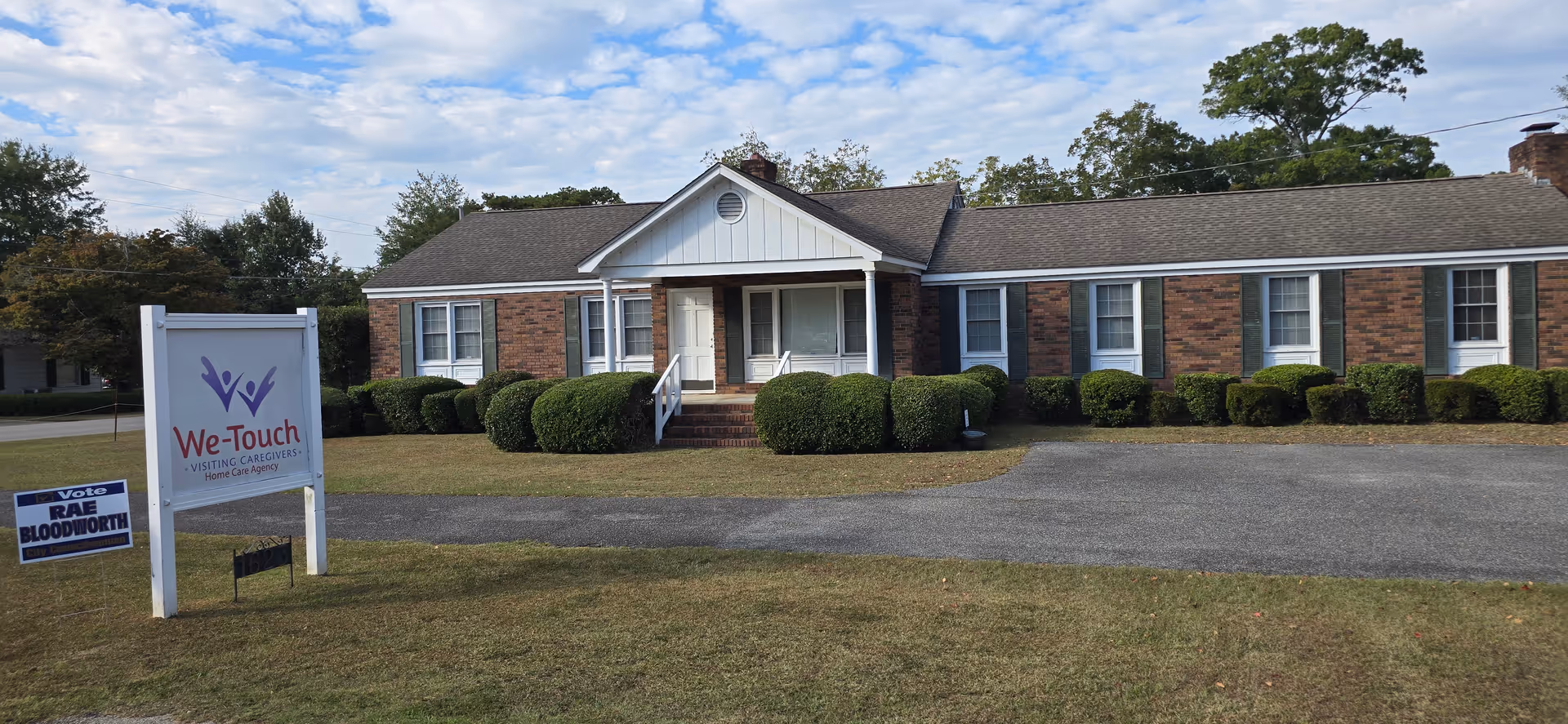 Single-story brick facility with front entrance, trimmed shrubs, and a We-Touch sign.