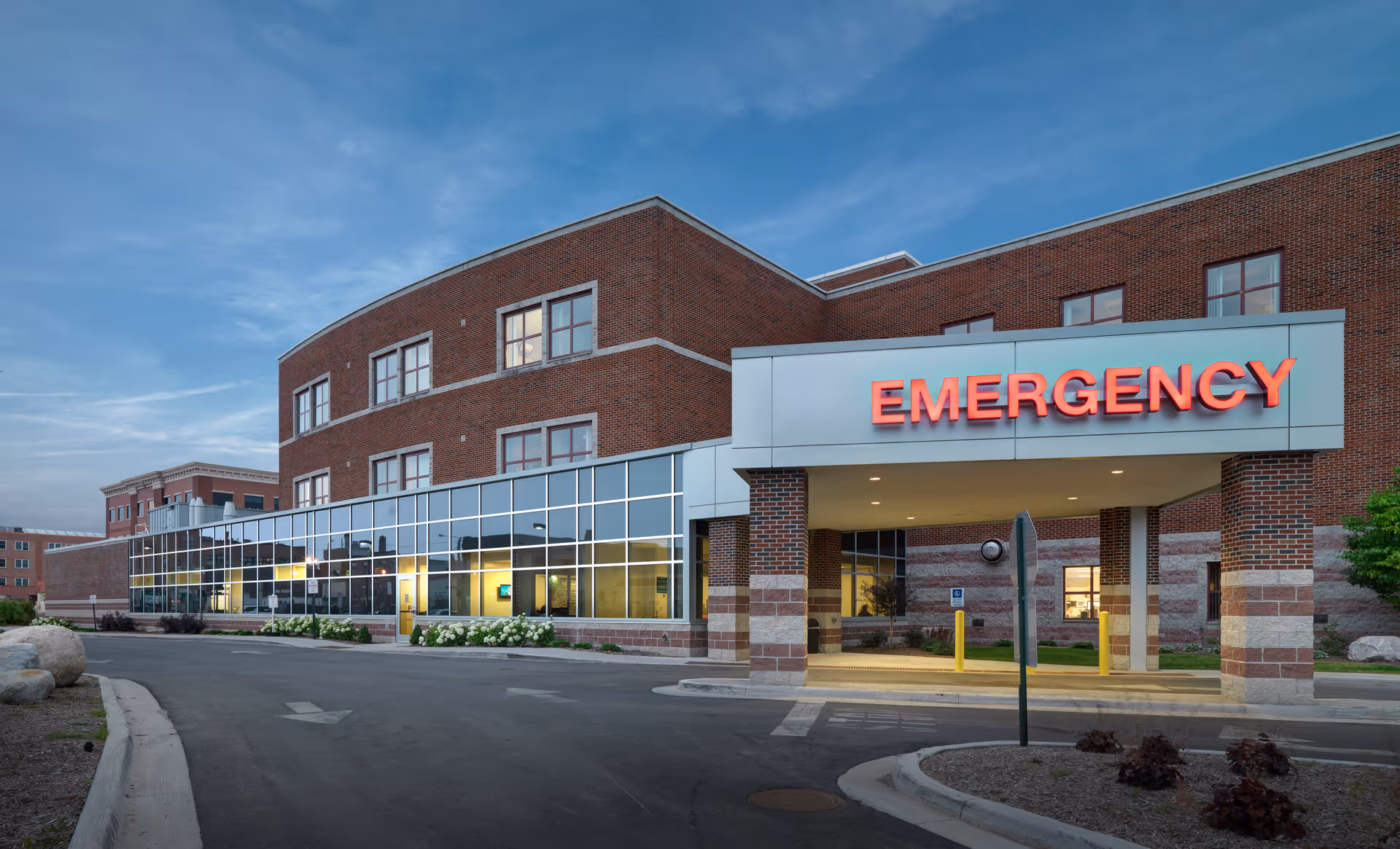 Exterior view of hospital entrance with bright EMERGENCY sign and glass facade.