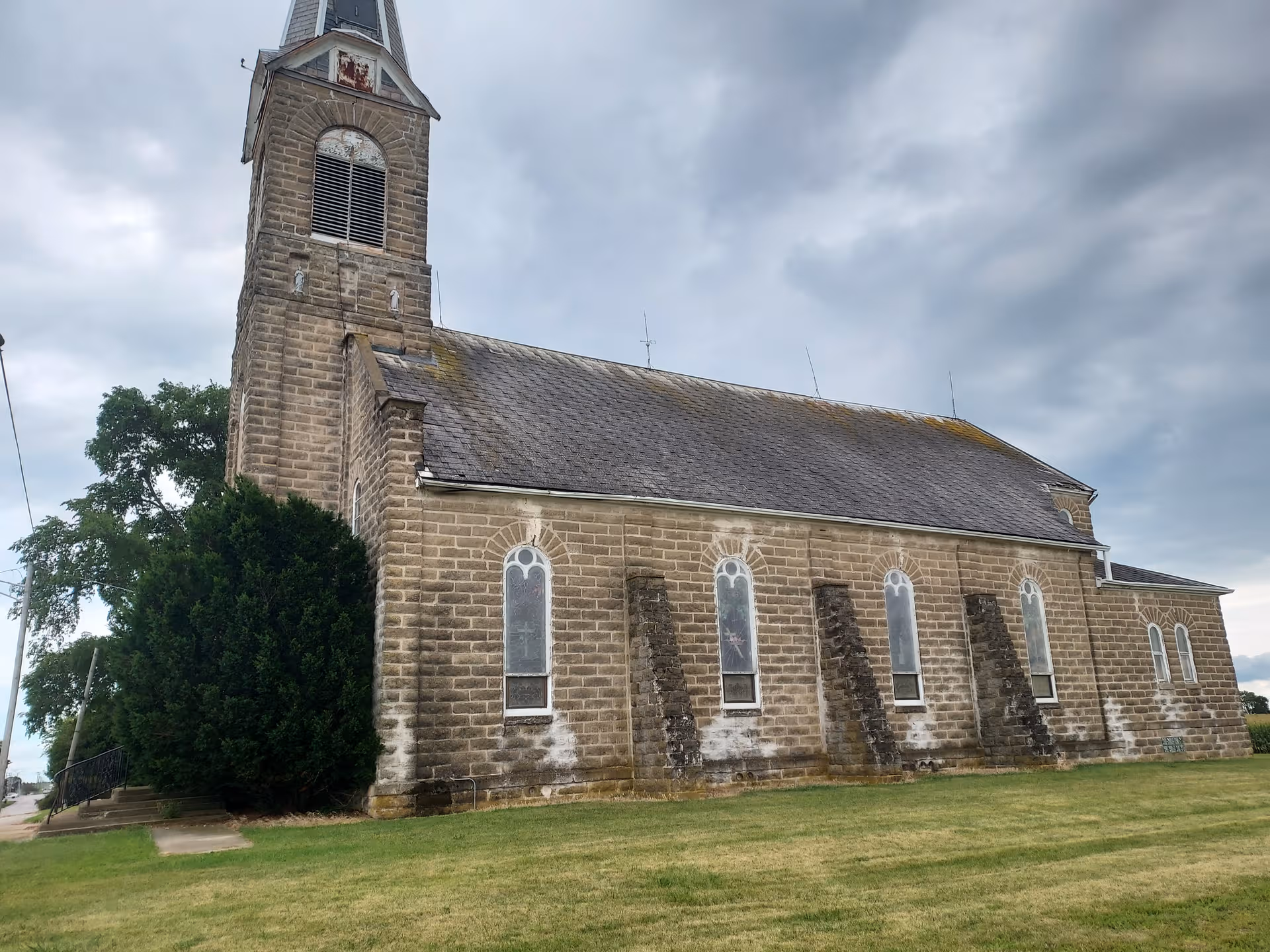 Stone church-like building with a tall steeple, arched windows, on a grassy lawn.